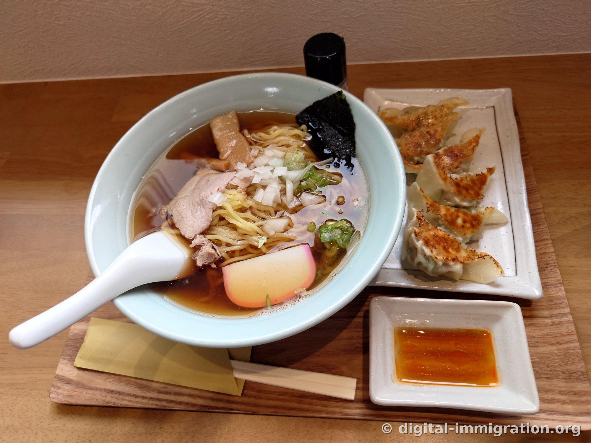 木のトレーに乗った醤油ラーメンと焼いた餃子五個、赤いラー油ソースが入った小皿