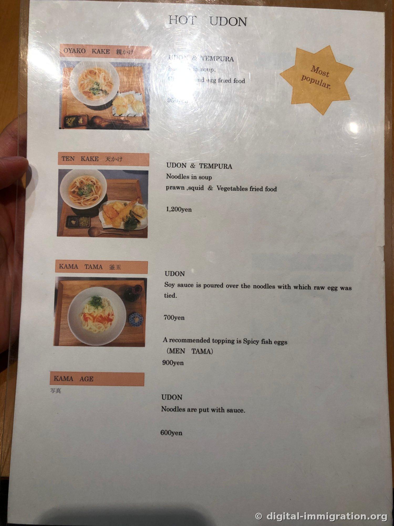 HOT UDONと書かれた英語メニュー板、おやこかけ・てんかけ・かまたま・かまあげの写真と価格が書かれていて、右上にMost popular星マークがある