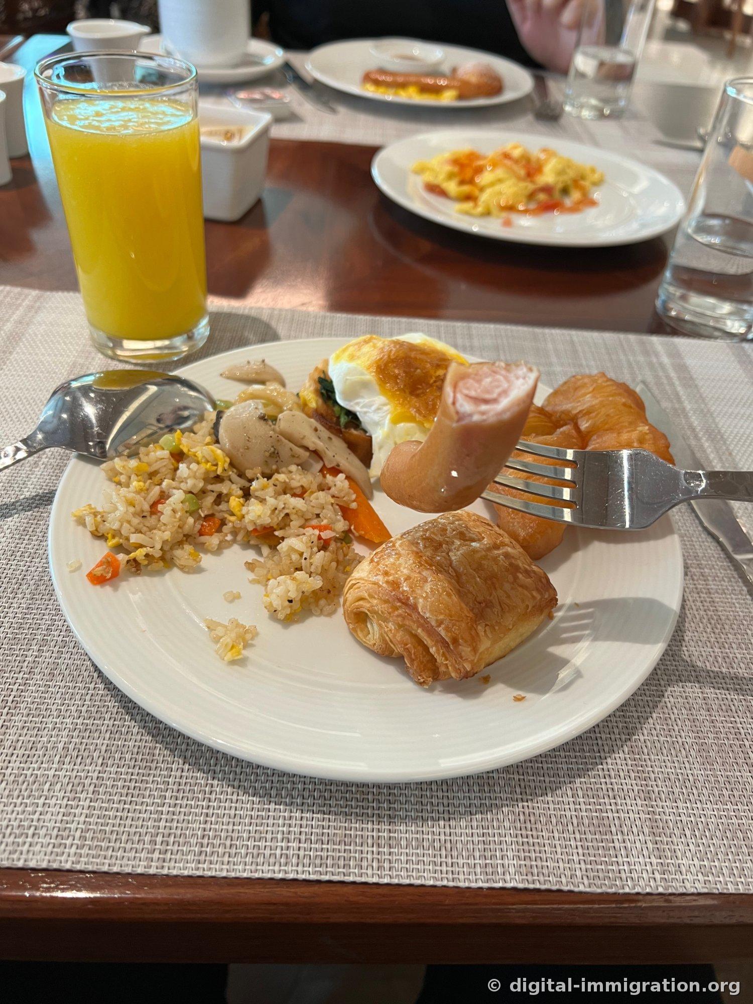 Assiette blanche avec riz sauté, champignons sautés, toast avec œuf à moitié cuit, saucisse, croissant et verre de jus d'orange à côté