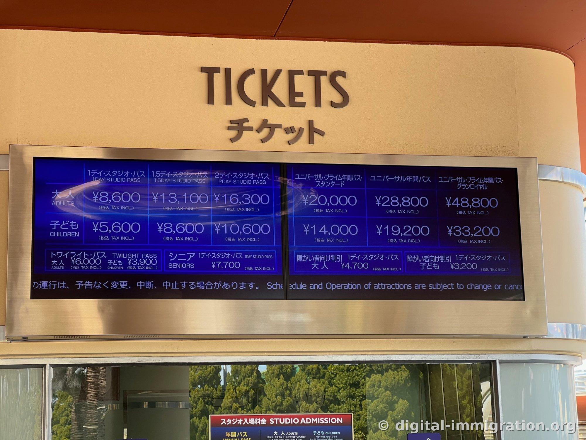 Digital display above the TICKETS booth showing admission prices: 1-Day Studio Pass Adult 8600 yen and other ticket options