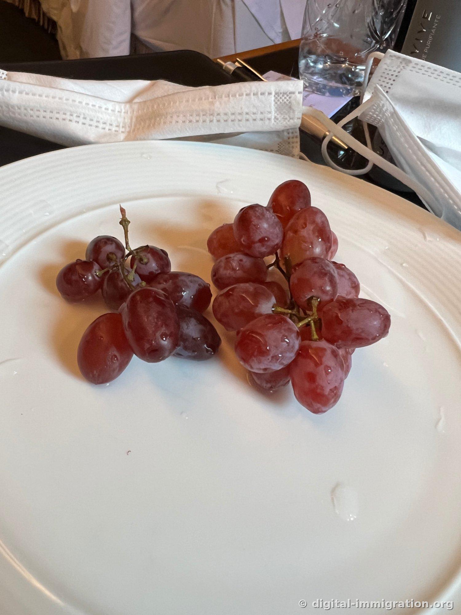 Assiette blanche avec deux grappes de raisins rouges humides, serviette et bouteille d'eau en arrière-plan sur une table de chambre