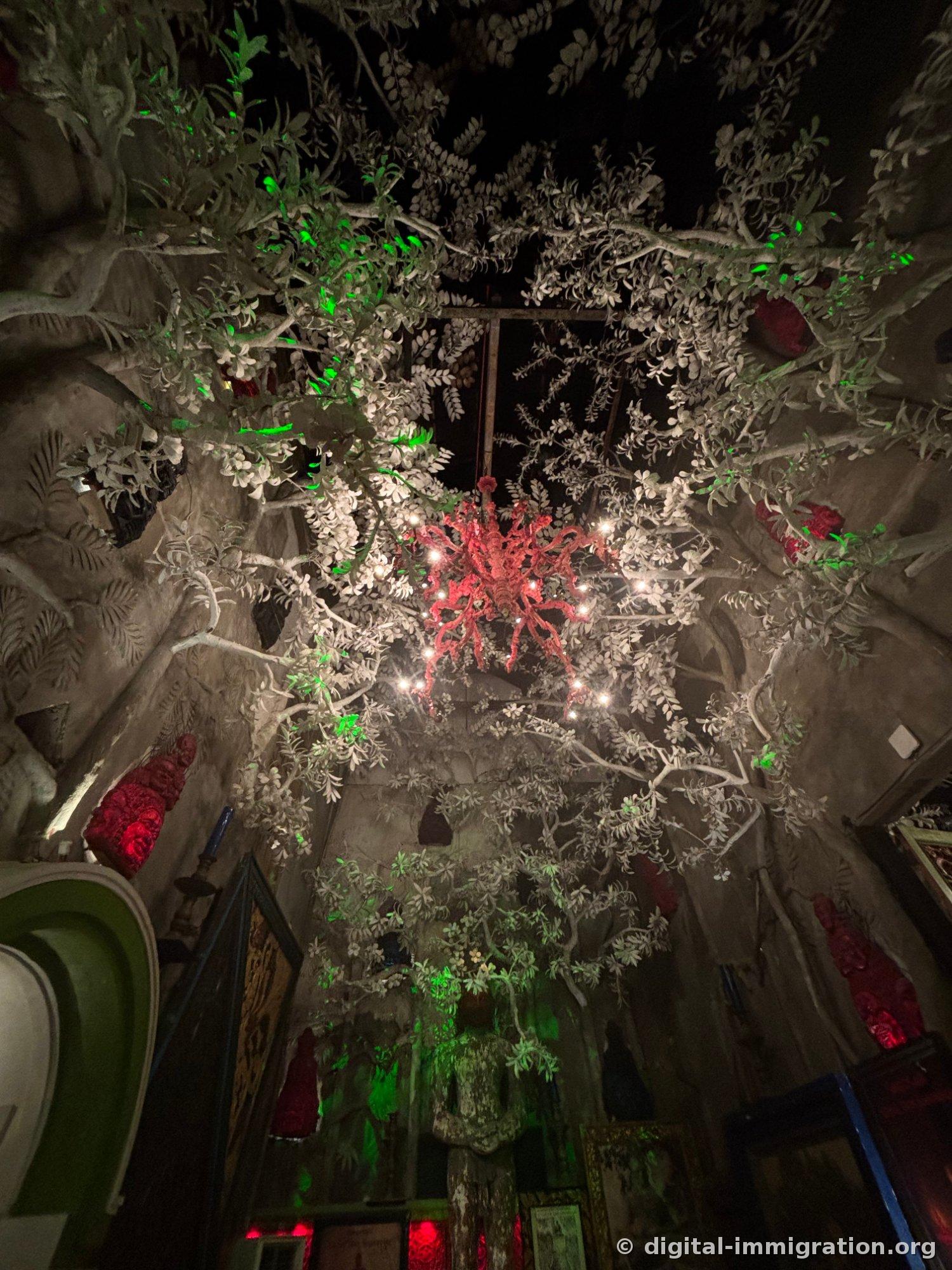 Looking up at concrete tree ceiling with green lighting and red coral-shaped chandelier suspended in center