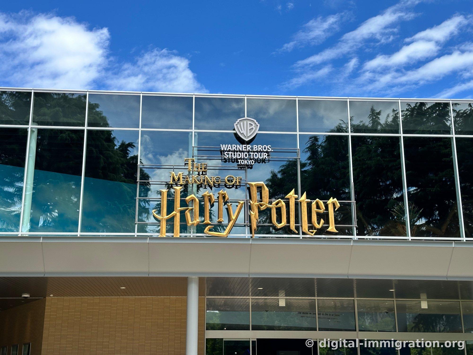 A building exterior with a gold Harry Potter logo and WARNER BROS. STUDIO TOUR TOKYO sign on a glass wall under blue sky