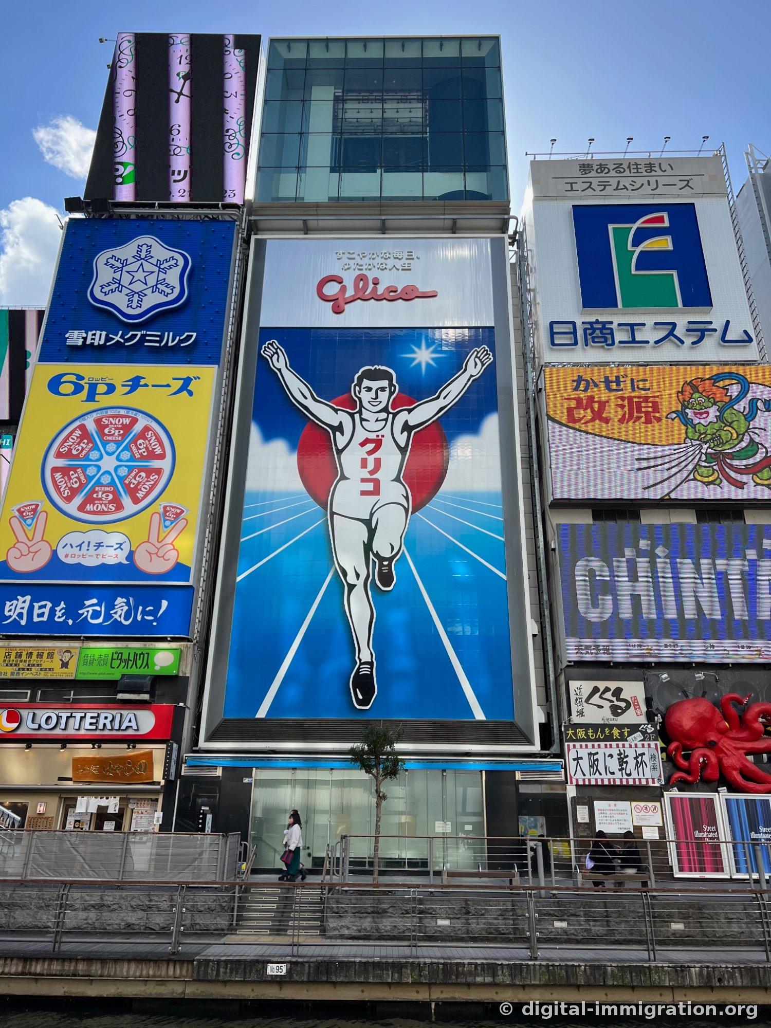 Le coureur Glico et les enseignes 6P Cheese, Yukijirushi Megmilk, Lotteria à côté, vus sous un ciel bleu le jour
