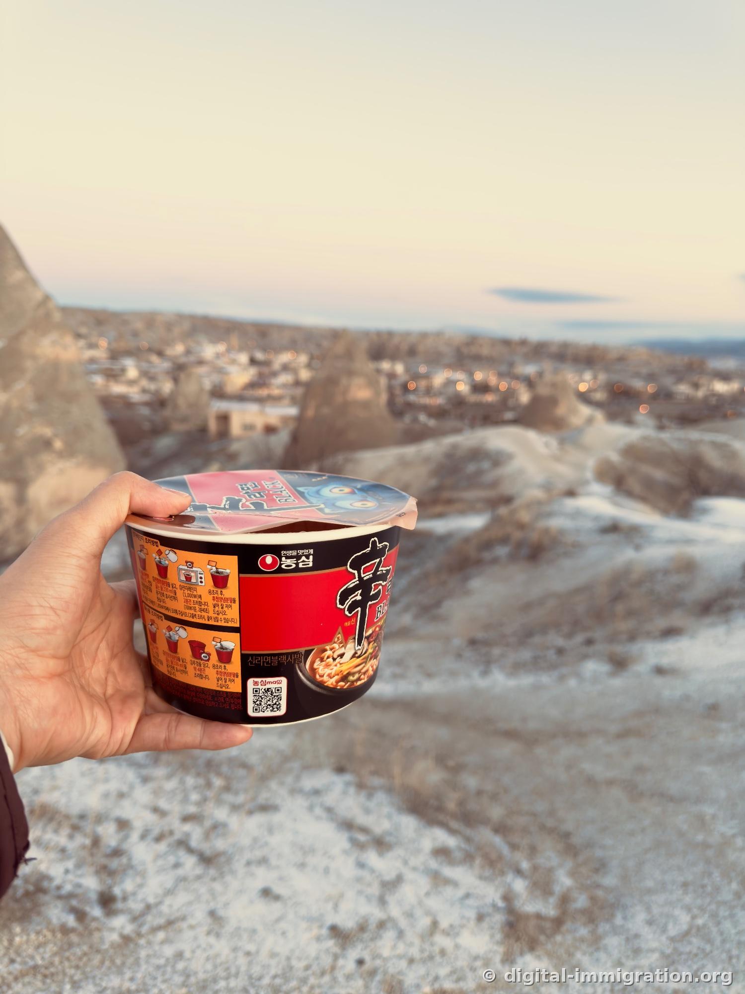Tenez un bol de Shin Ramyun Black Nongshim dans vos mains sur la colline, derrière le village de Göreme éclairé à la lumière de l'aube et les cheminées de fée, le sol couvert de givre