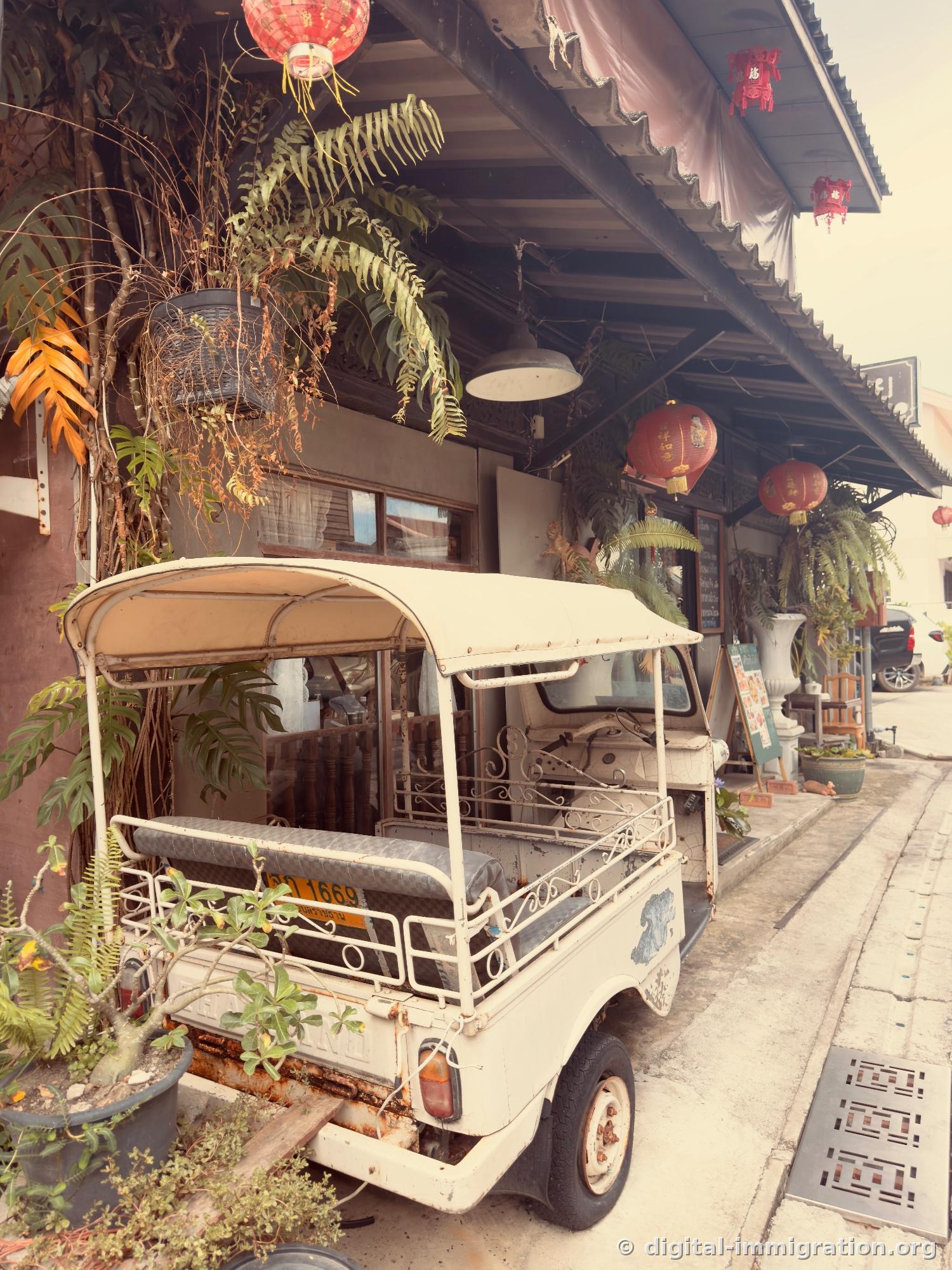 White vintage tuk-tuk parked in front of shop with red Chinese lantern and potted plants under eaves