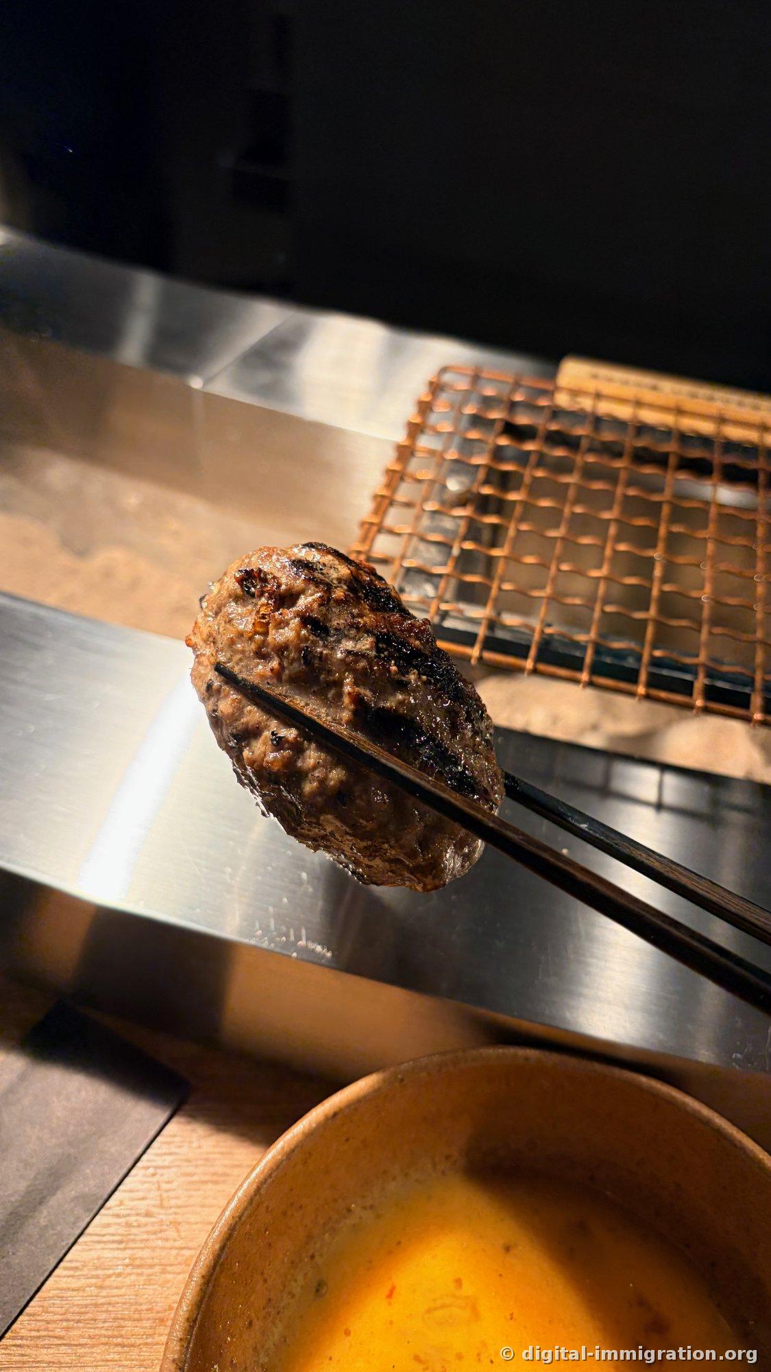 Un hamburger saisi avec les baguettes, le plateau en treillis de cuivre derrière, et un bol de sauce jaune en dessous
