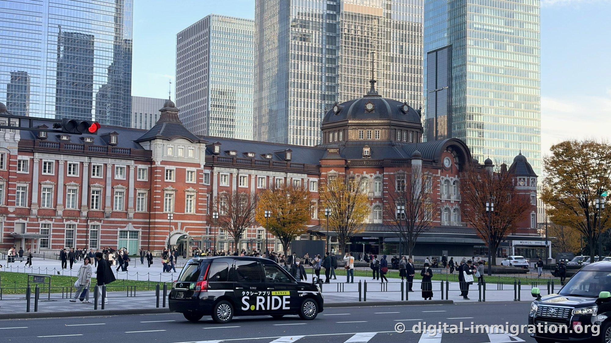 Un taxi noir portant le logo S.RIDE passant devant la route du dôme sud de la Gare de Tokyo, avec les visiteurs réunis sur la place