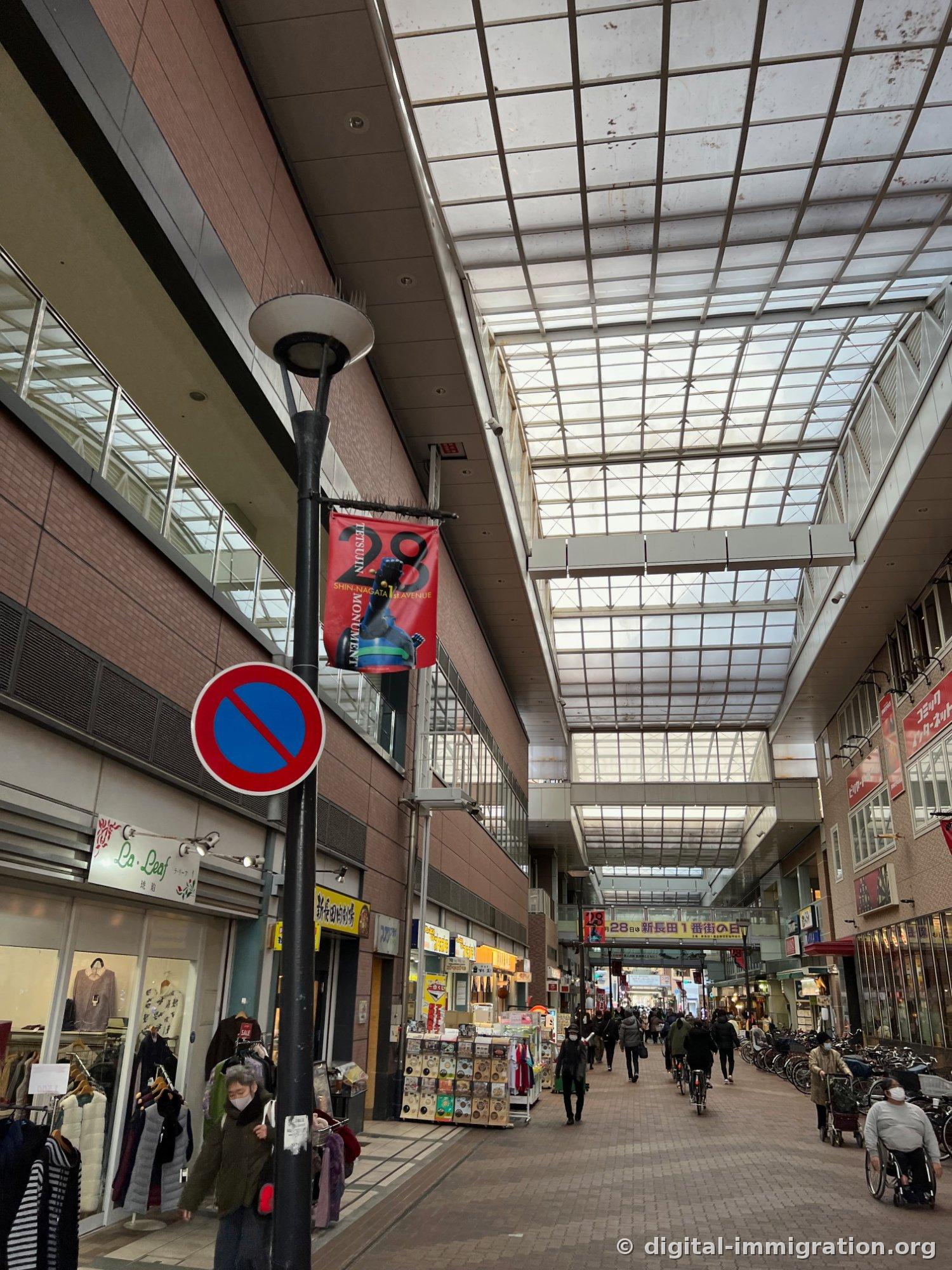 Une galerie marchande couverte de verre avec la galerie Shin-Nagata 1st Avenue, avec des bannières de Tetsujin 28 accrochées aux lampadaires