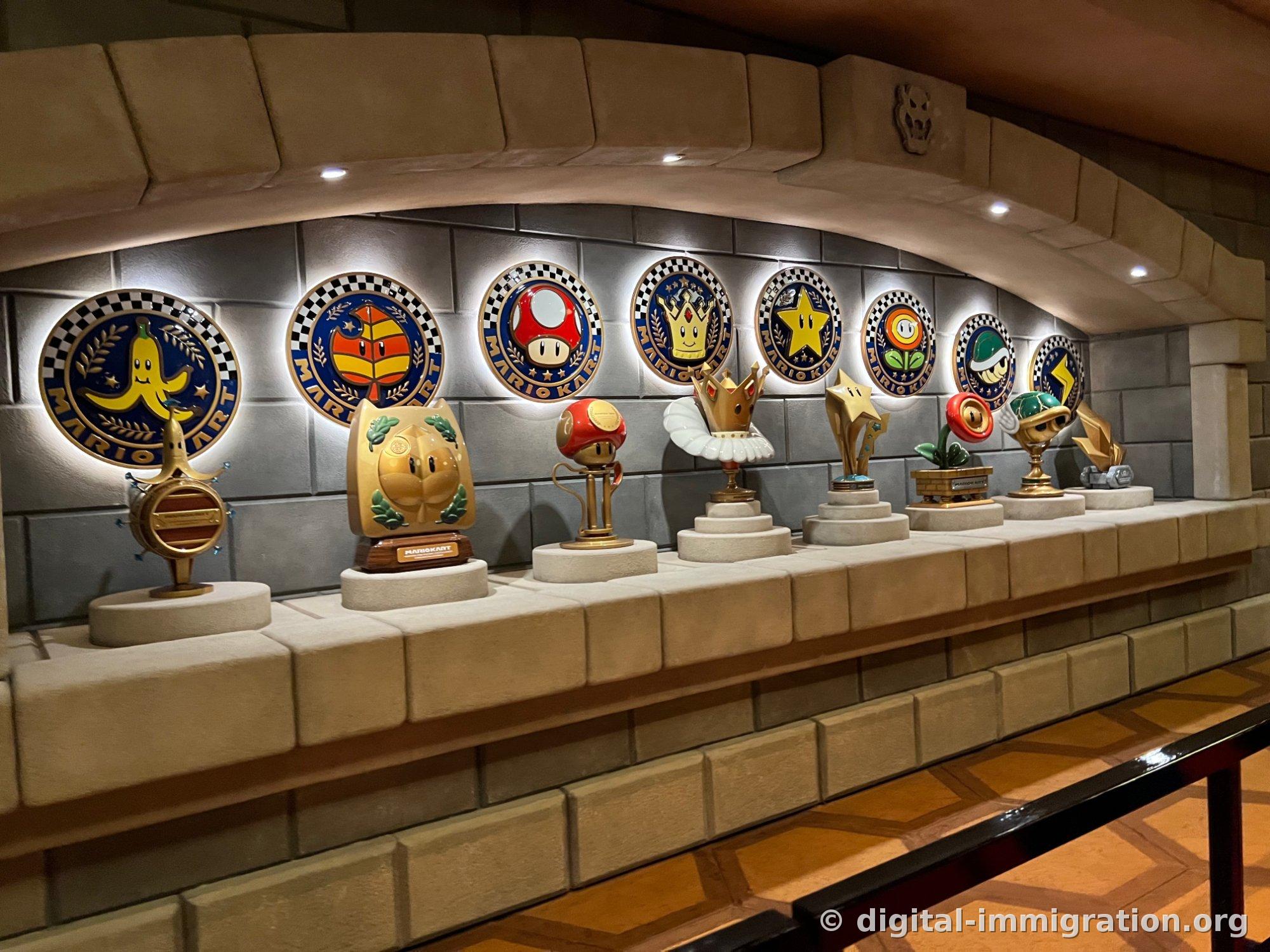 Mario Kart trophy display. Banana, leaf, mushroom, crown, star, fire flower, shell, and lightning-shaped trophies are lit and arranged in a row