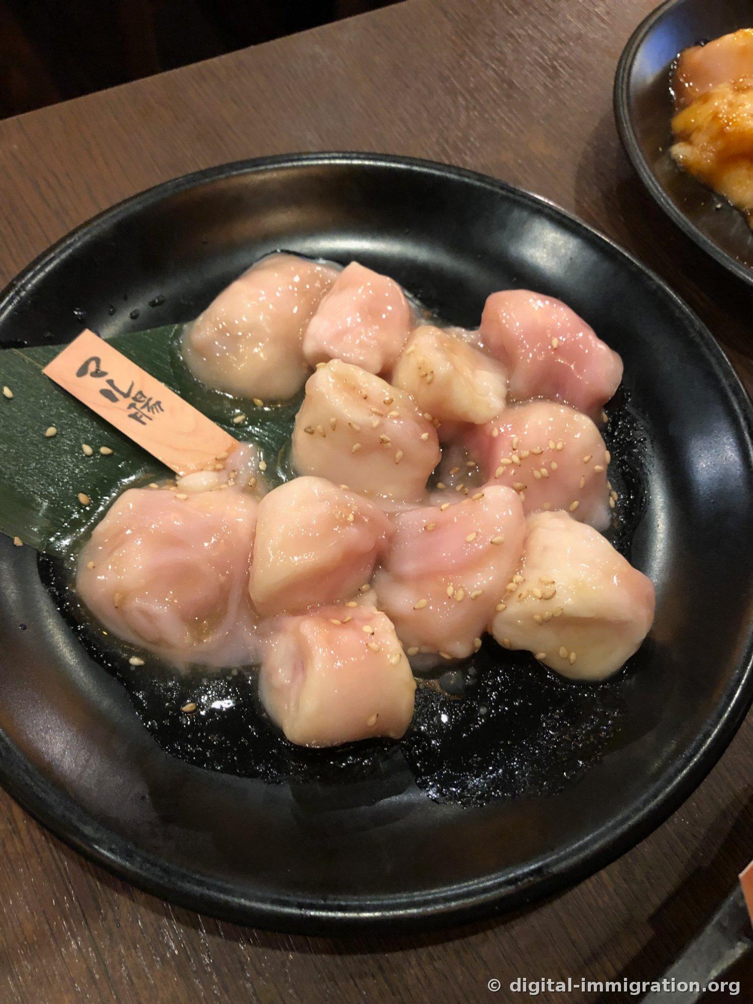 Morceaux de tripes crues dans une assiette noire, saupoudrés de graines de sésame avec une étiquette en bois plantée