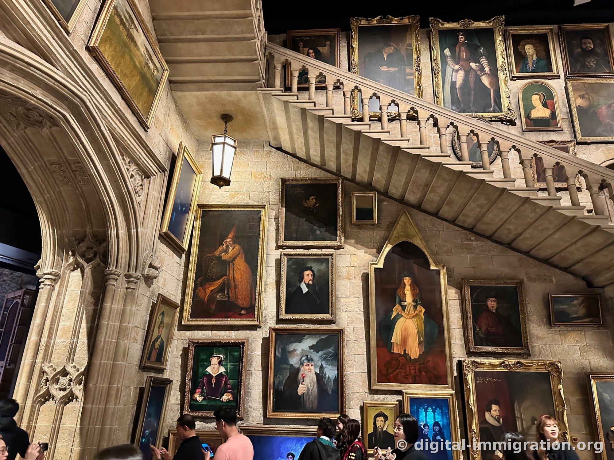 Dozens of gold-framed portrait paintings in various sizes densely hung on a wall beside a stone staircase
