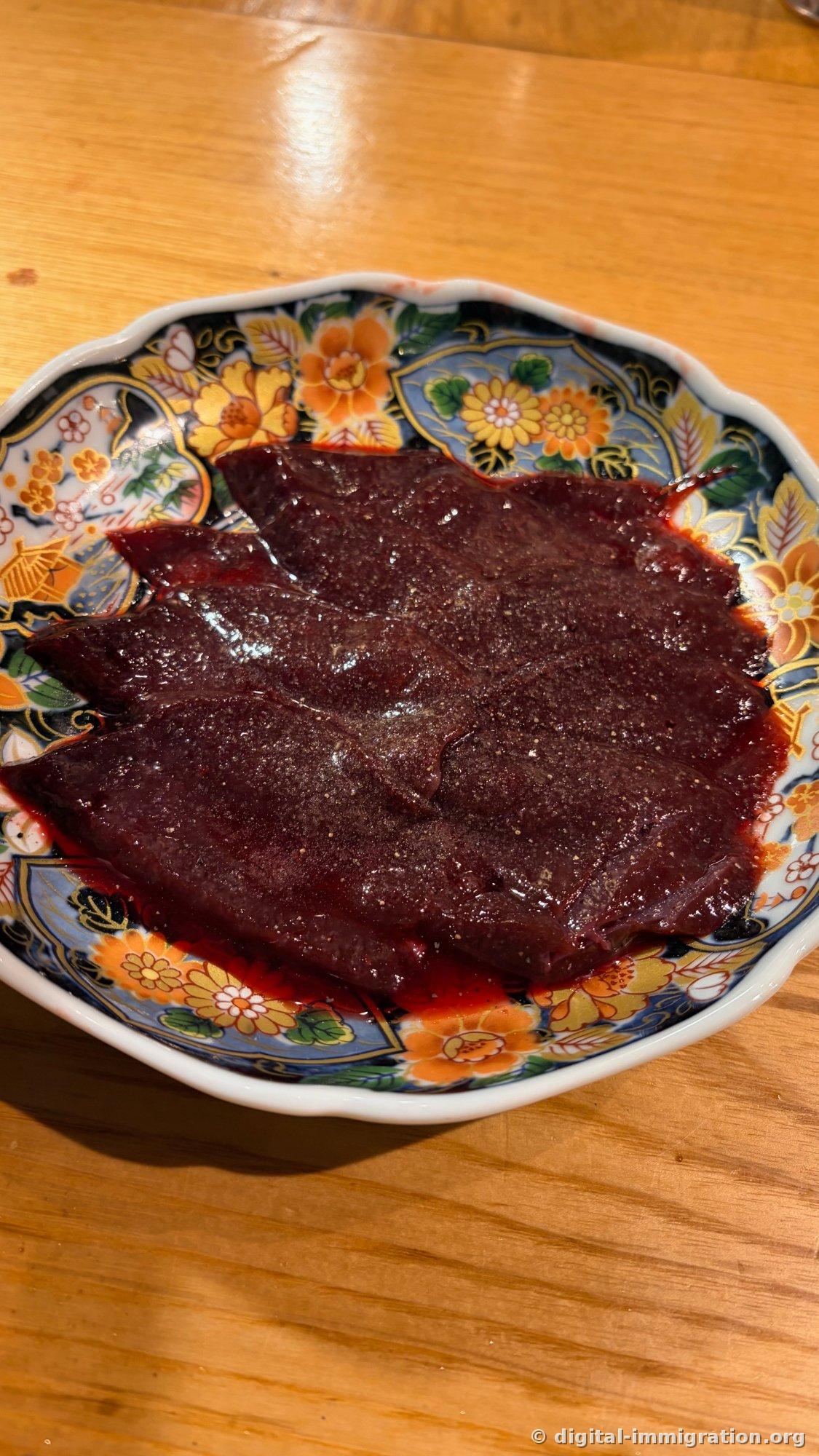 Sliced beef liver on a Japanese ceramic plate with floral patterns. Coarse pepper is sprinkled over the surface