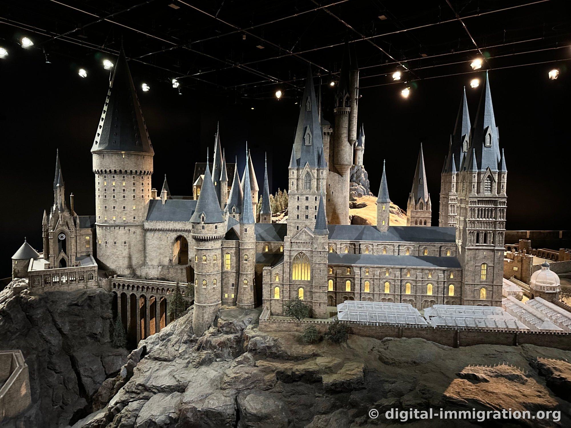 A detailed Hogwarts castle model under lighting with lit windows and a glass greenhouse visible on the right