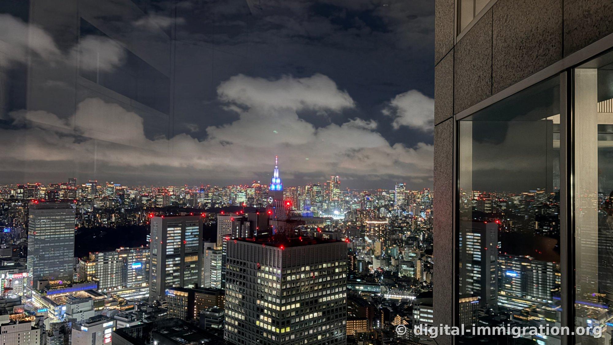 Bâtiment NTT docomo Yoyogi avec sa flèche bleue sous un ciel nocturne nuageux et paysage urbain nocturne vers l'est de Tokyo