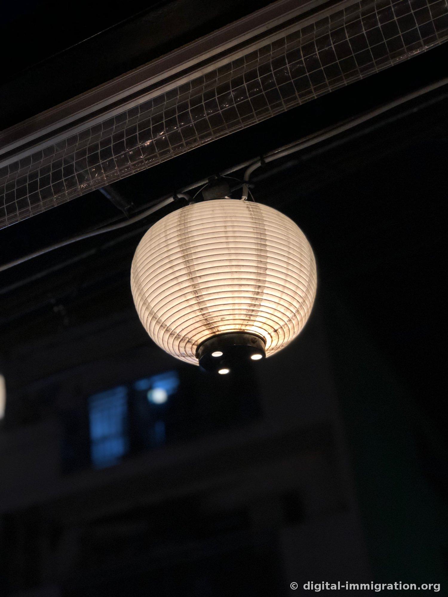 黑暗的夜晚，屋檐下孤独亮起的圆形白色纸灯笼特写