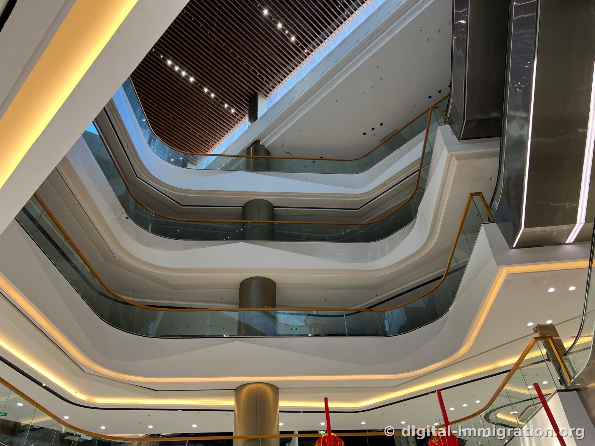 Vue de l'atrium du Parkson Mall regardé de bas en haut, avec les rampes de 4 étages reliées par des mains courantes en laiton courbées et le plafond en lames de bois