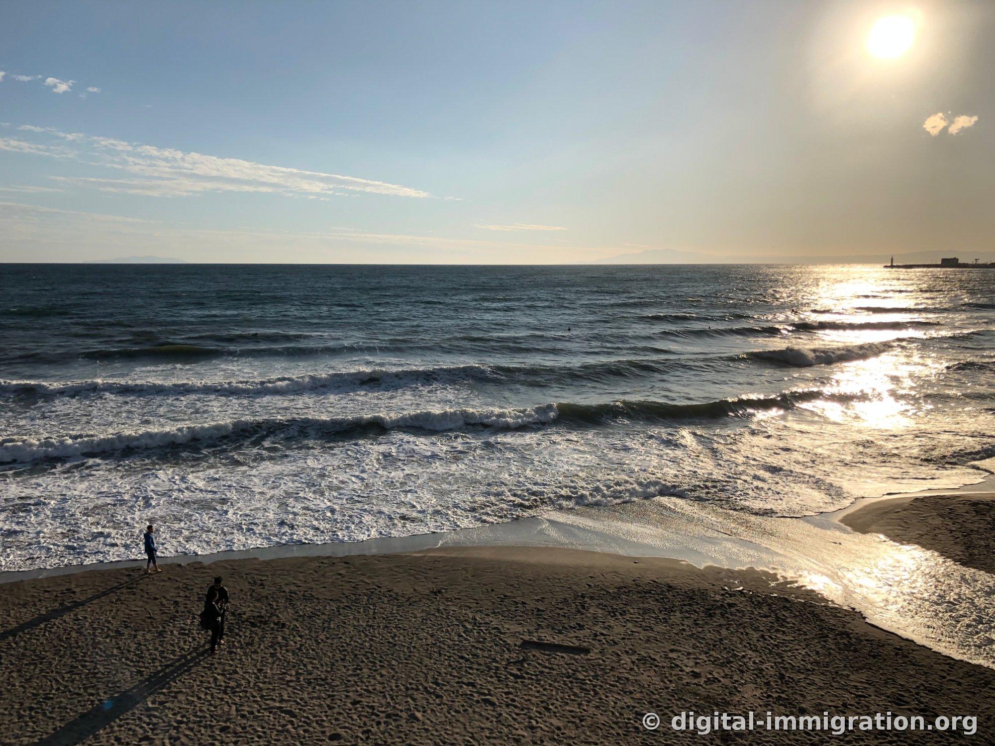La surface de la mer brille en or avec le soleil en haut à droite et les vagues arrivent en plusieurs couches, paysage de la Baie de Sagami
