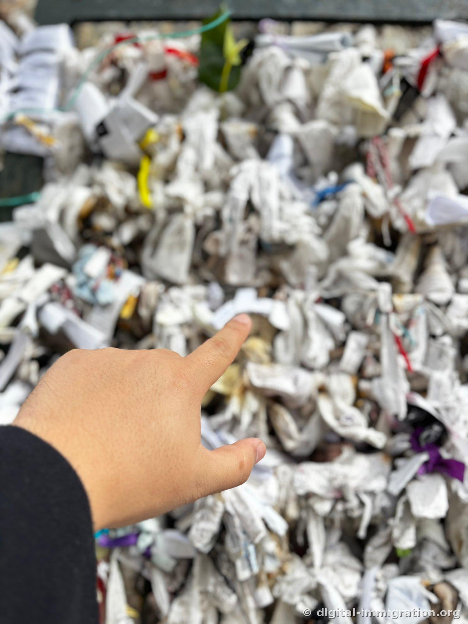 A person in a black-sleeved shirt points to white paper knots densely tied on the wish wall