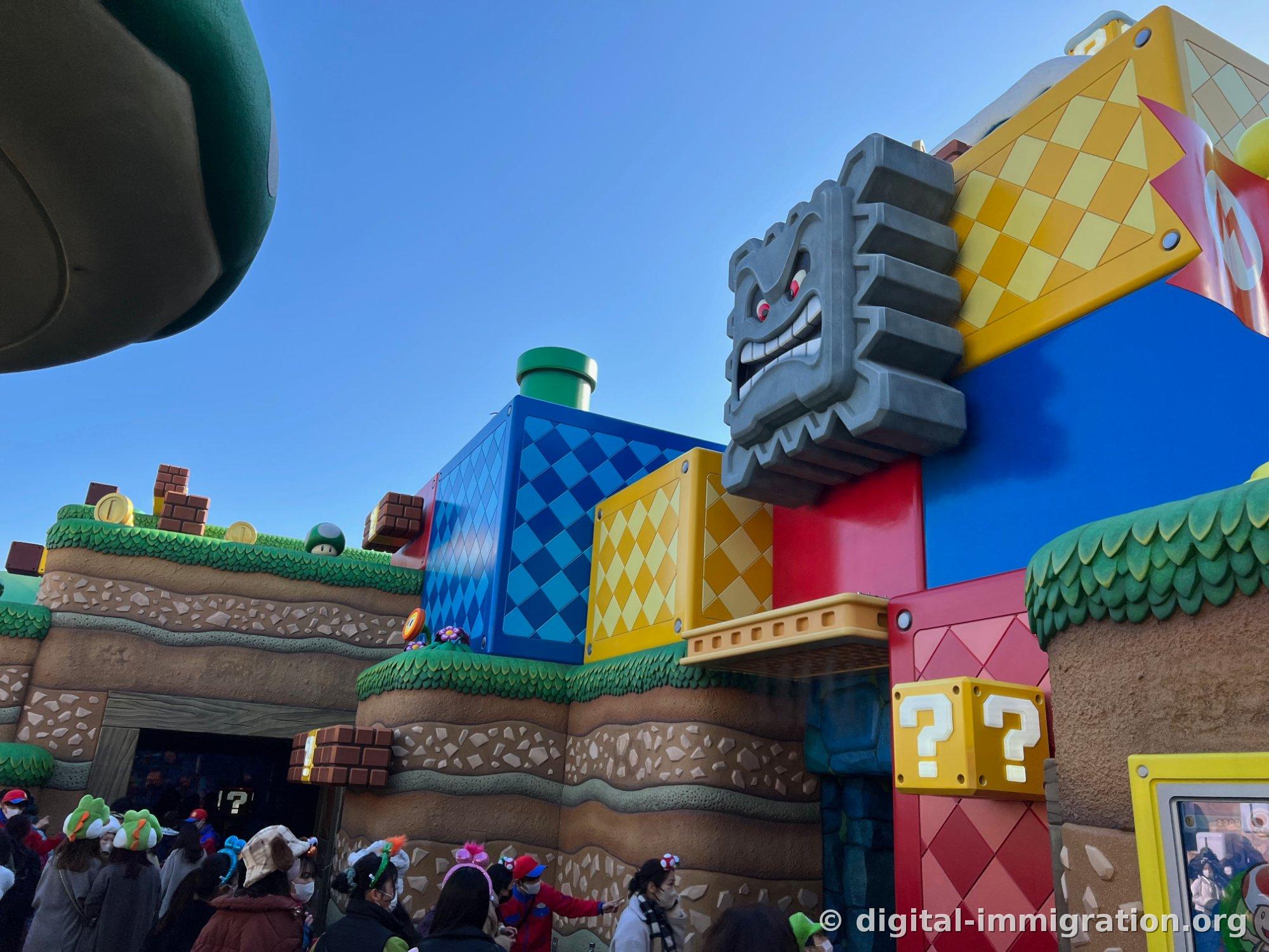 Viewed from below: blue and yellow diamond-patterned blocks, a gray stone face character with exposed teeth, and two yellow question mark blocks