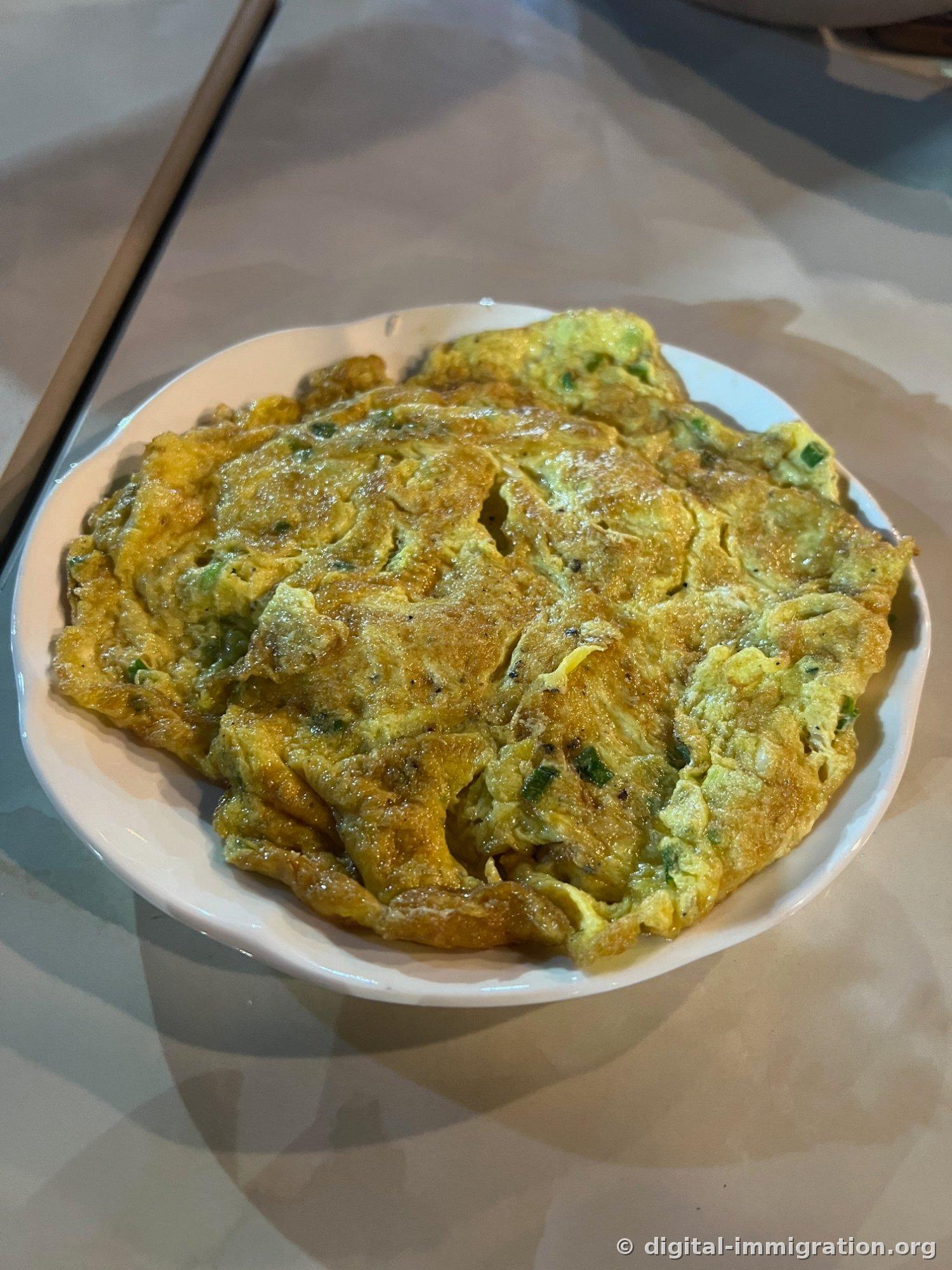 边缘蓬松起来的老挝式蛋卷盛在白色盘子上，左边放着木筷子