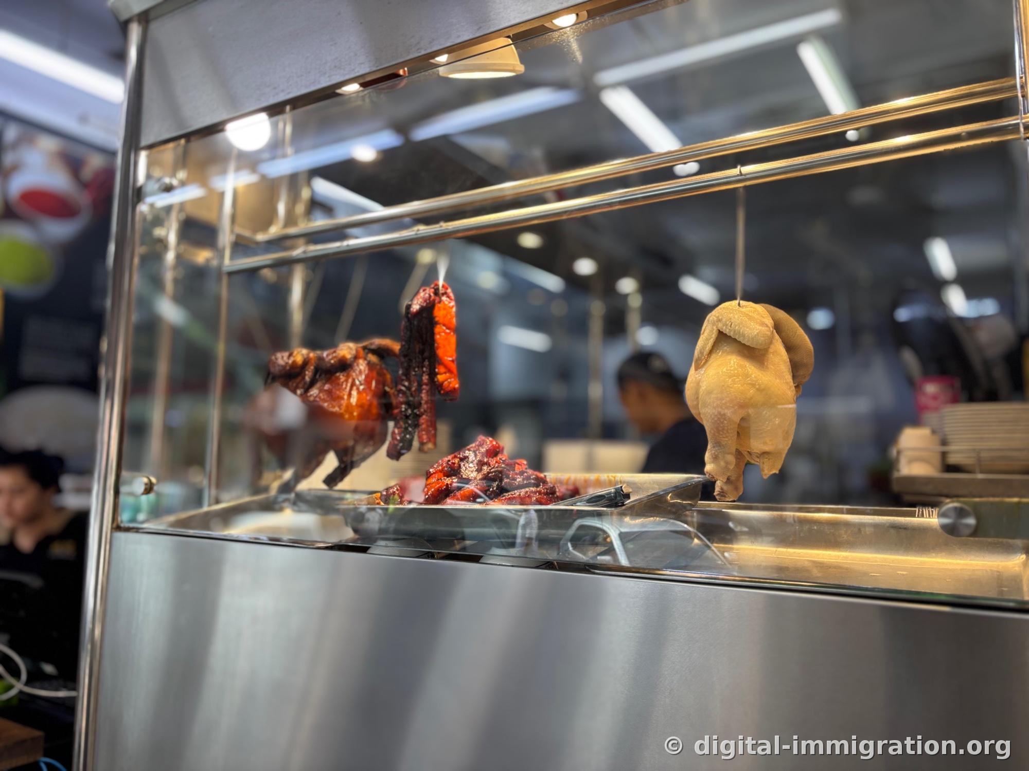 Inside a stainless steel display case hangs a pale steamed chicken, with reddish-roasted char siu and Chinese sausage