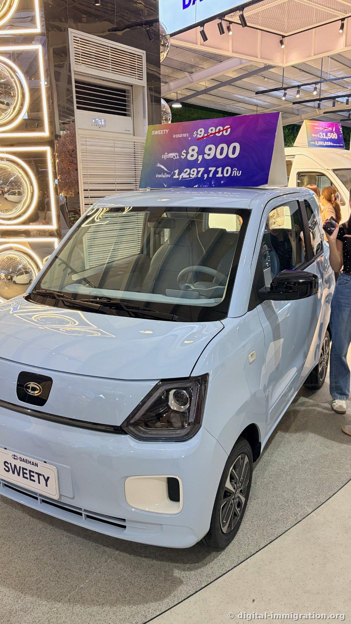 Light blue DAEHAN SWEETY compact EV with price tag showing discounted $8,900 from $9,900, 1,297,710 kip displayed