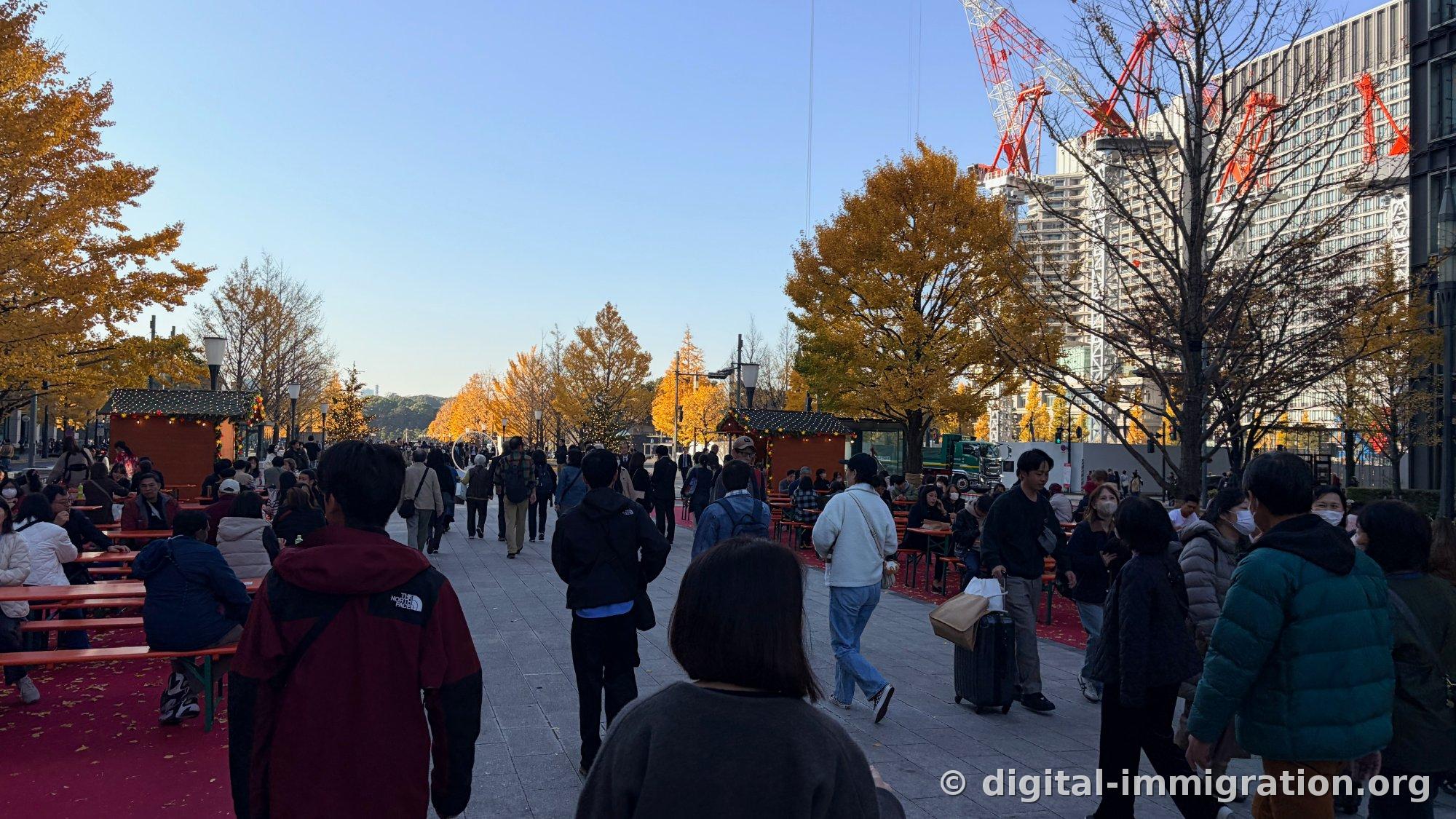 L'allée du marché de Noël remplie de monde avec les tables de banquet pliables sur le sol rouge, et la grue de construction rouge visible à l'arrière-droit