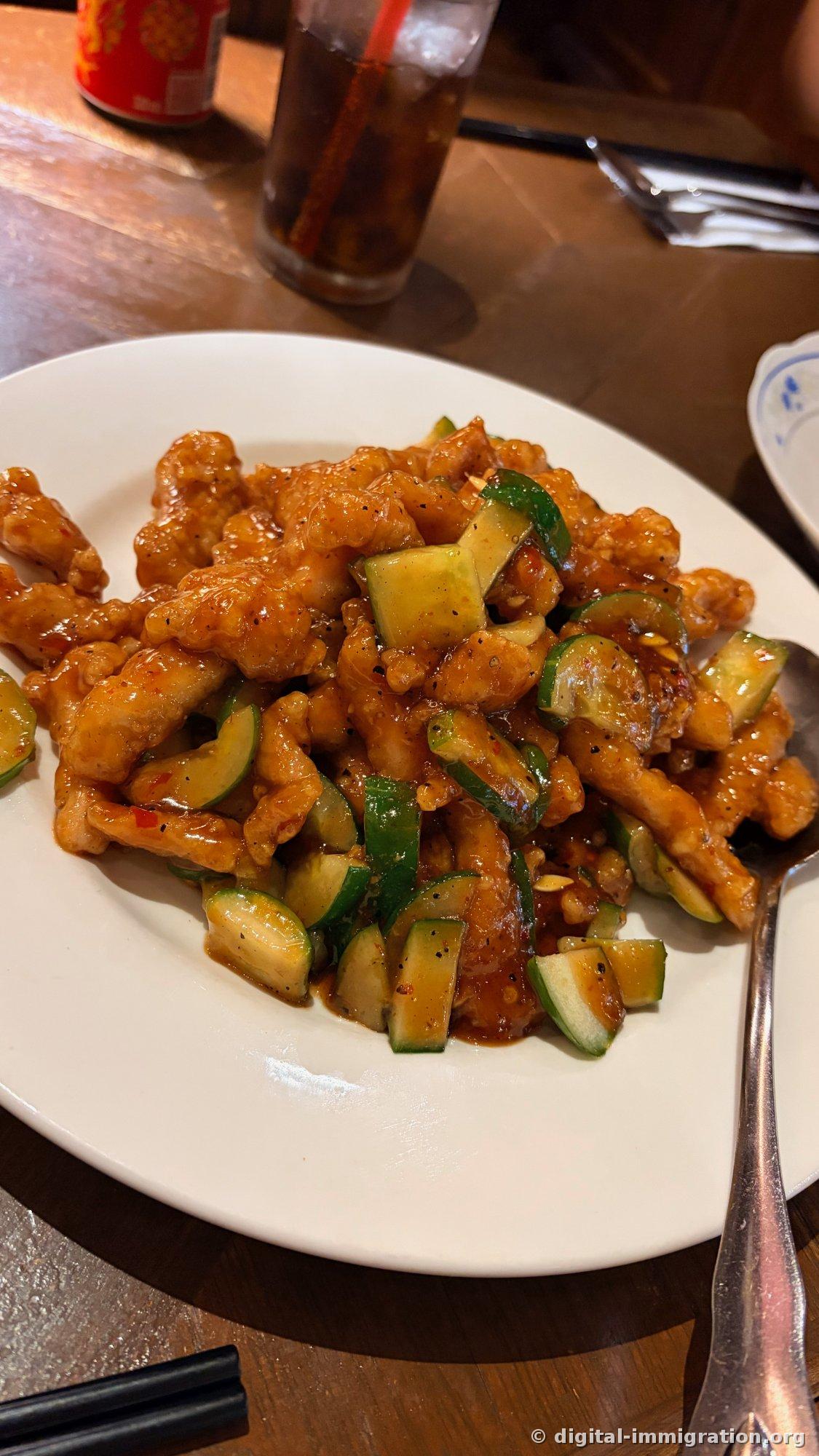 Fried meat and thick-cut cucumber stir-fried in a sweet-and-sour brown sauce on a white plate, with a cola glass beside it