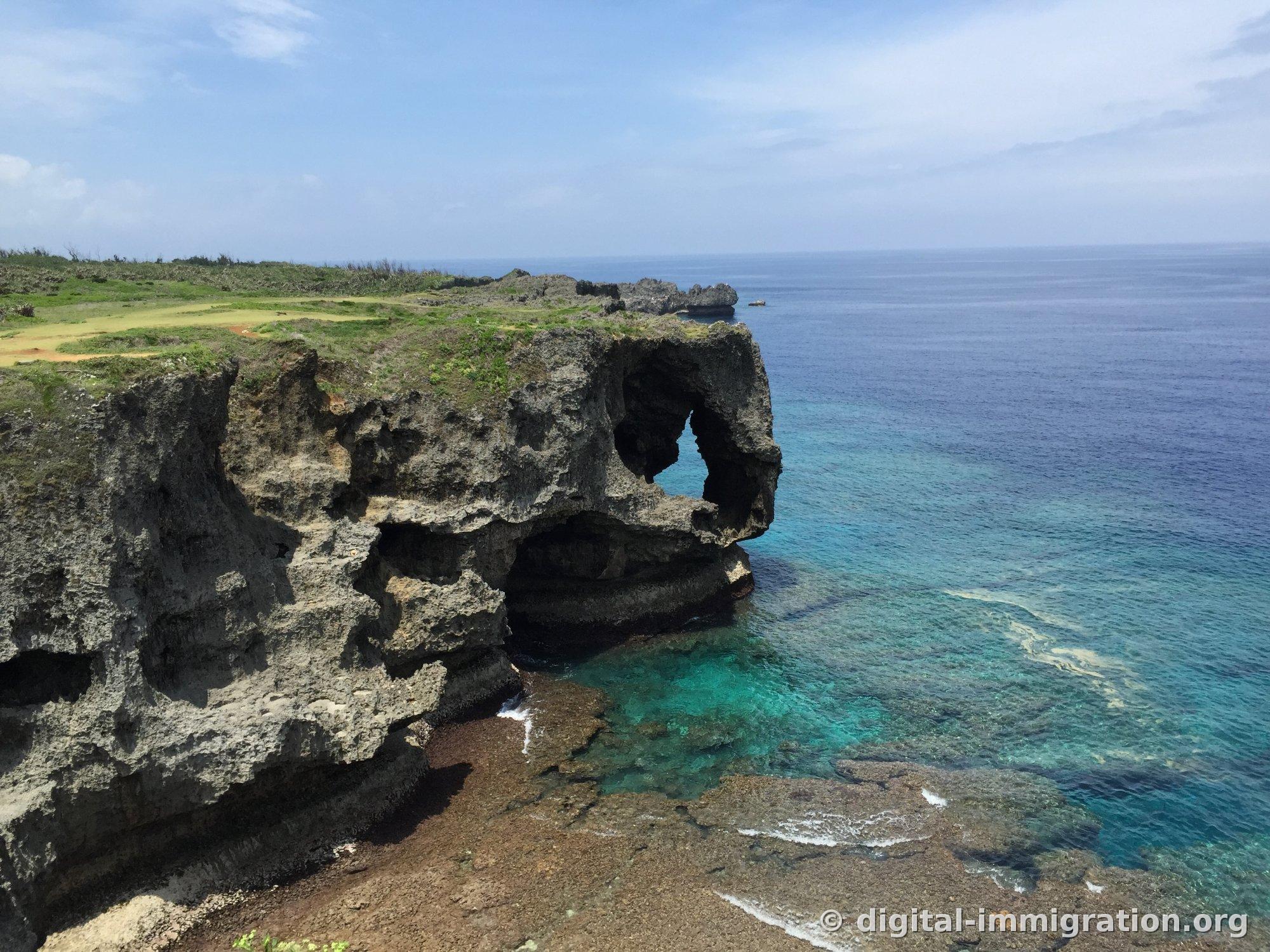 象が鼻を海に浸した姿に似た万座毛の石灰岩崖。岩の下のアーチ穴の間から海が見え、崖の上は緑の芝生で覆われている