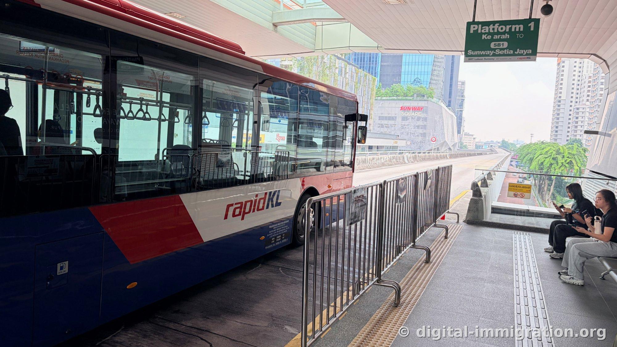 停在高架 BRT 站台的 rapidKL 涂装的红蓝公交车和'Platform 1 SB1 Sunway-Setia Jaya'绿色指示牌