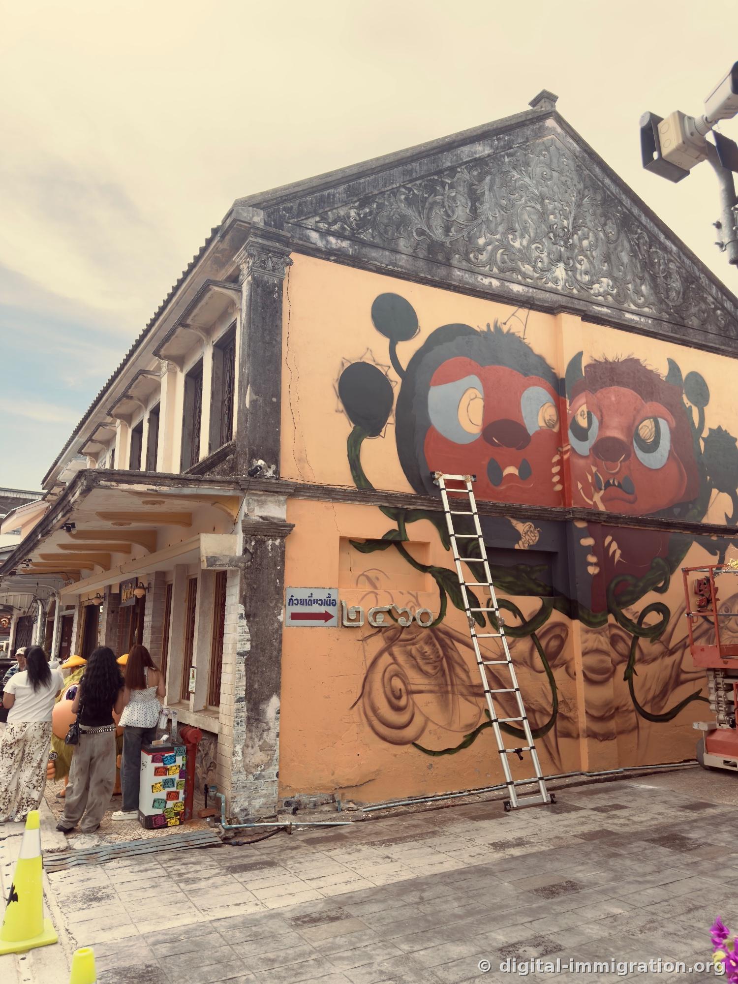 Corner building with large-eyed character mural on yellow wall with ladder and elevated work platform, arrow sign for beef noodle shop on lower left