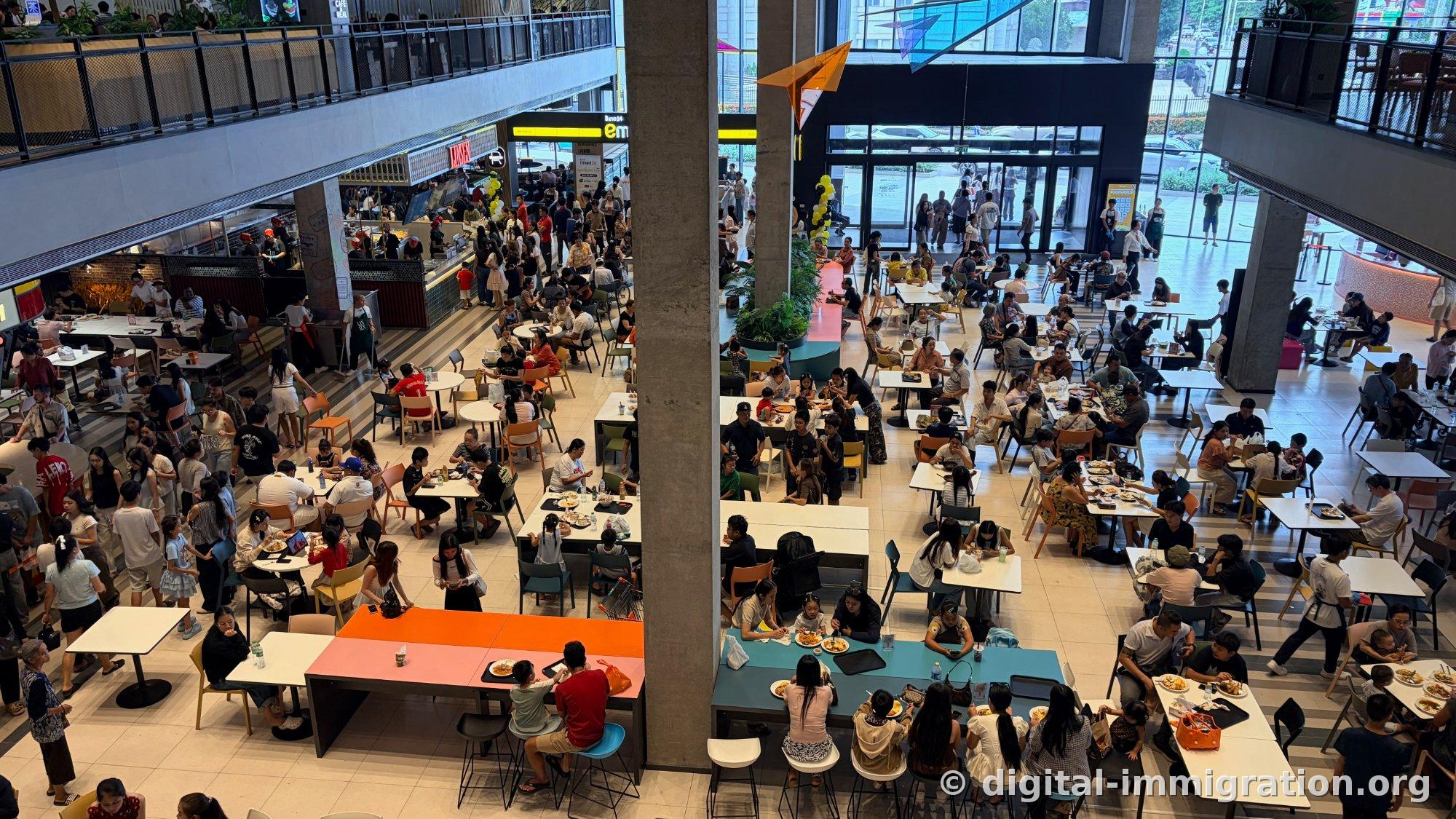 Large food court viewed from above with orange and mint-colored tables, families dining