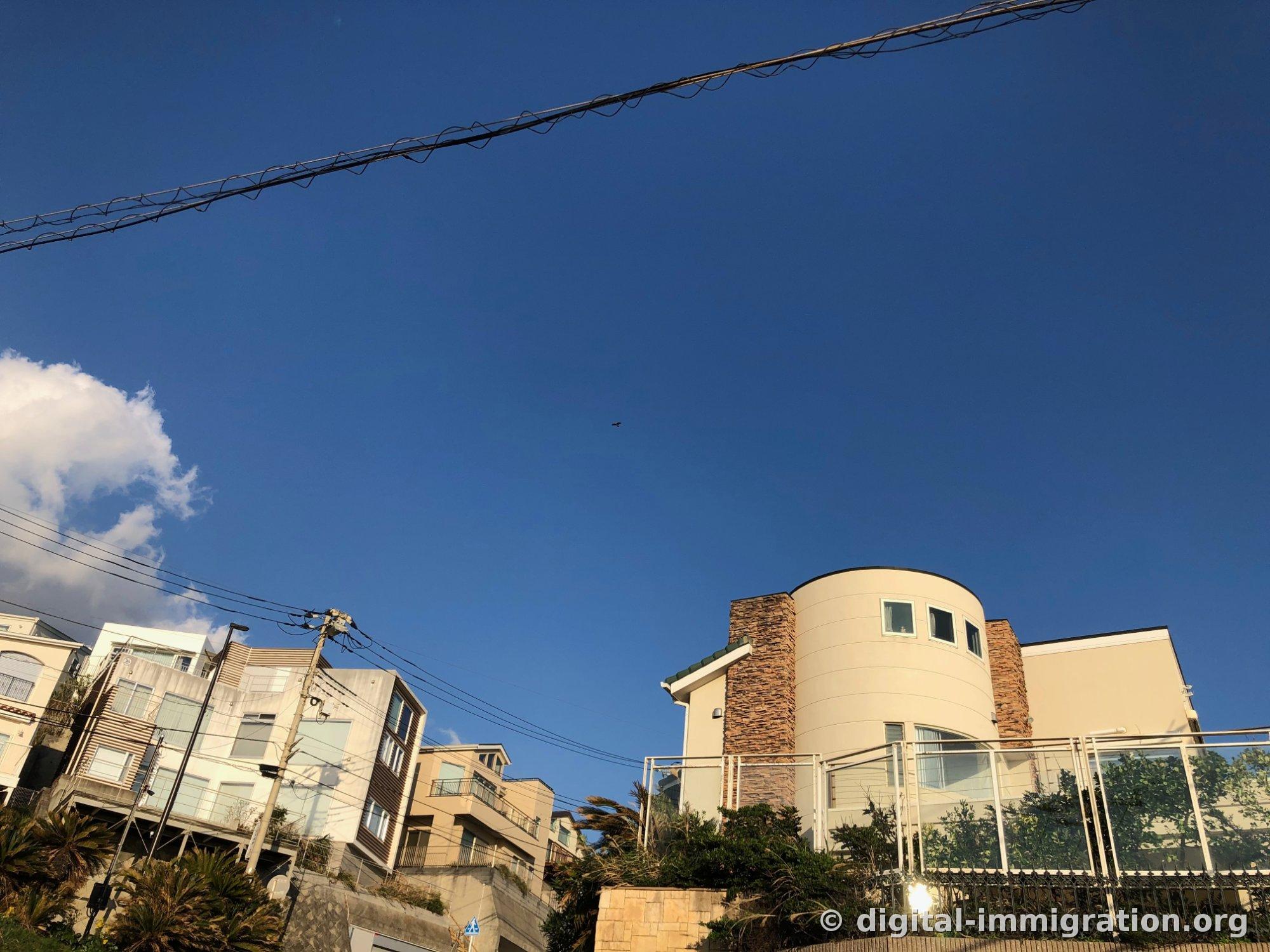 Sous les câbles de tramway traversant un ciel bleu foncé, des maisons sur la colline avec un mur arrondi et une balustrade en verre