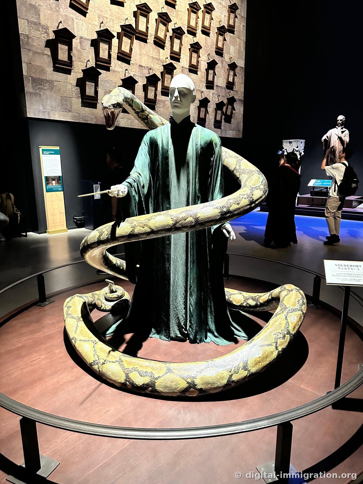 A Voldemort mannequin in teal robes on a circular platform with a large yellow serpent coiled around it