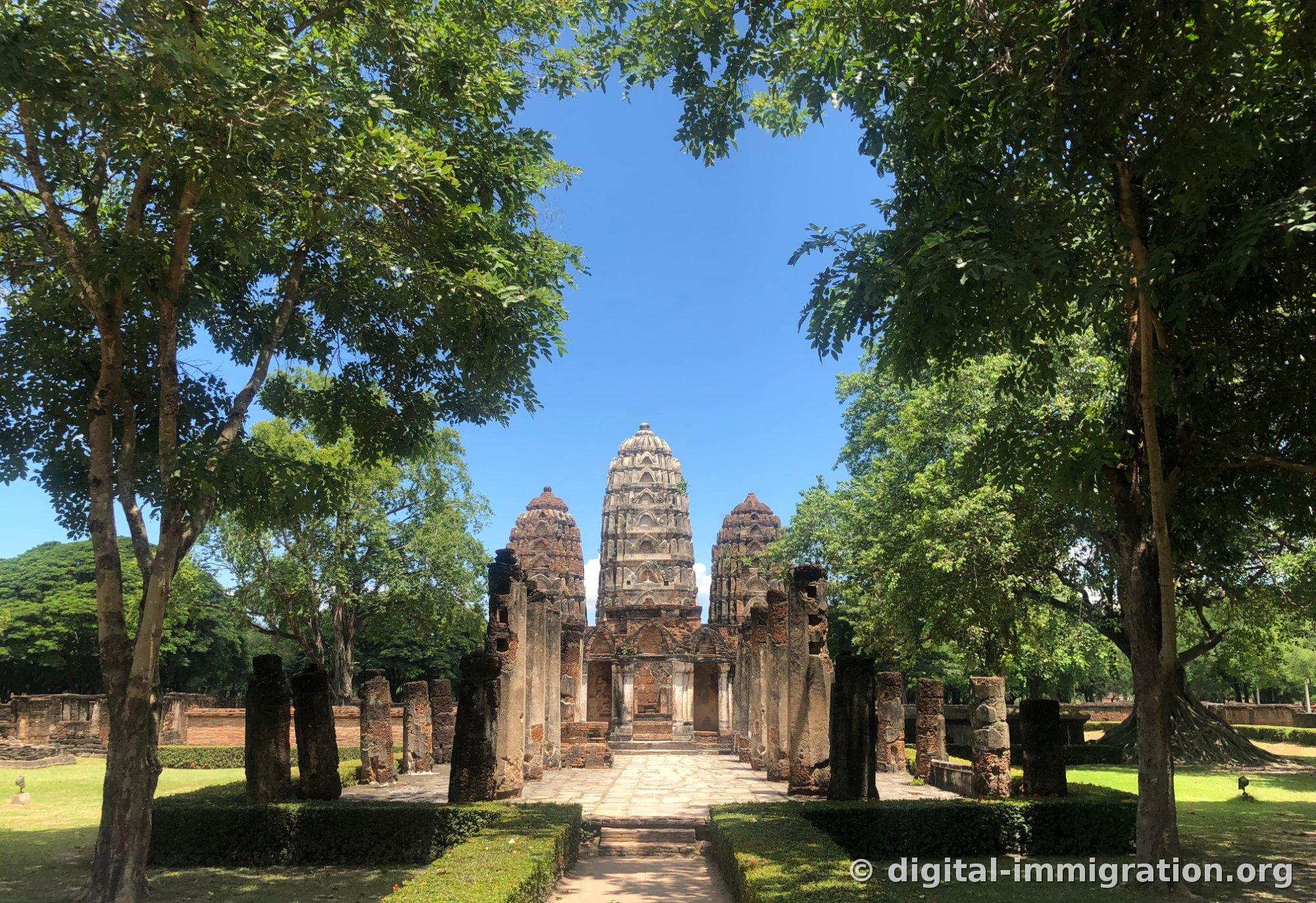 Three Khmer-style prangs of Wat Si Sawai standing at the end of a worship path framed by trees, with low columns on both sides