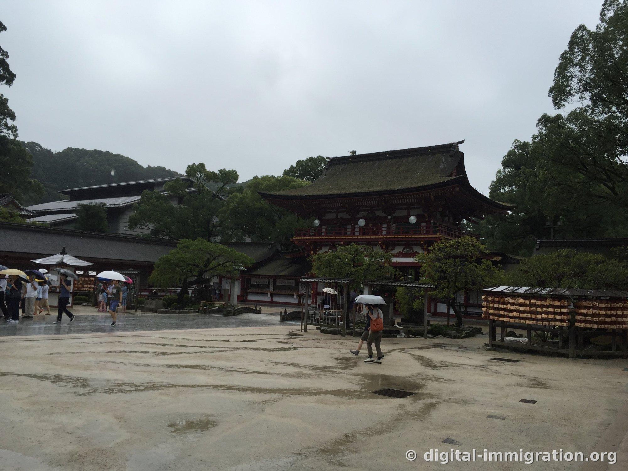 Romon gate viewed diagonally from the wide earthen grounds, densely packed wooden ema plaques hanging on the right