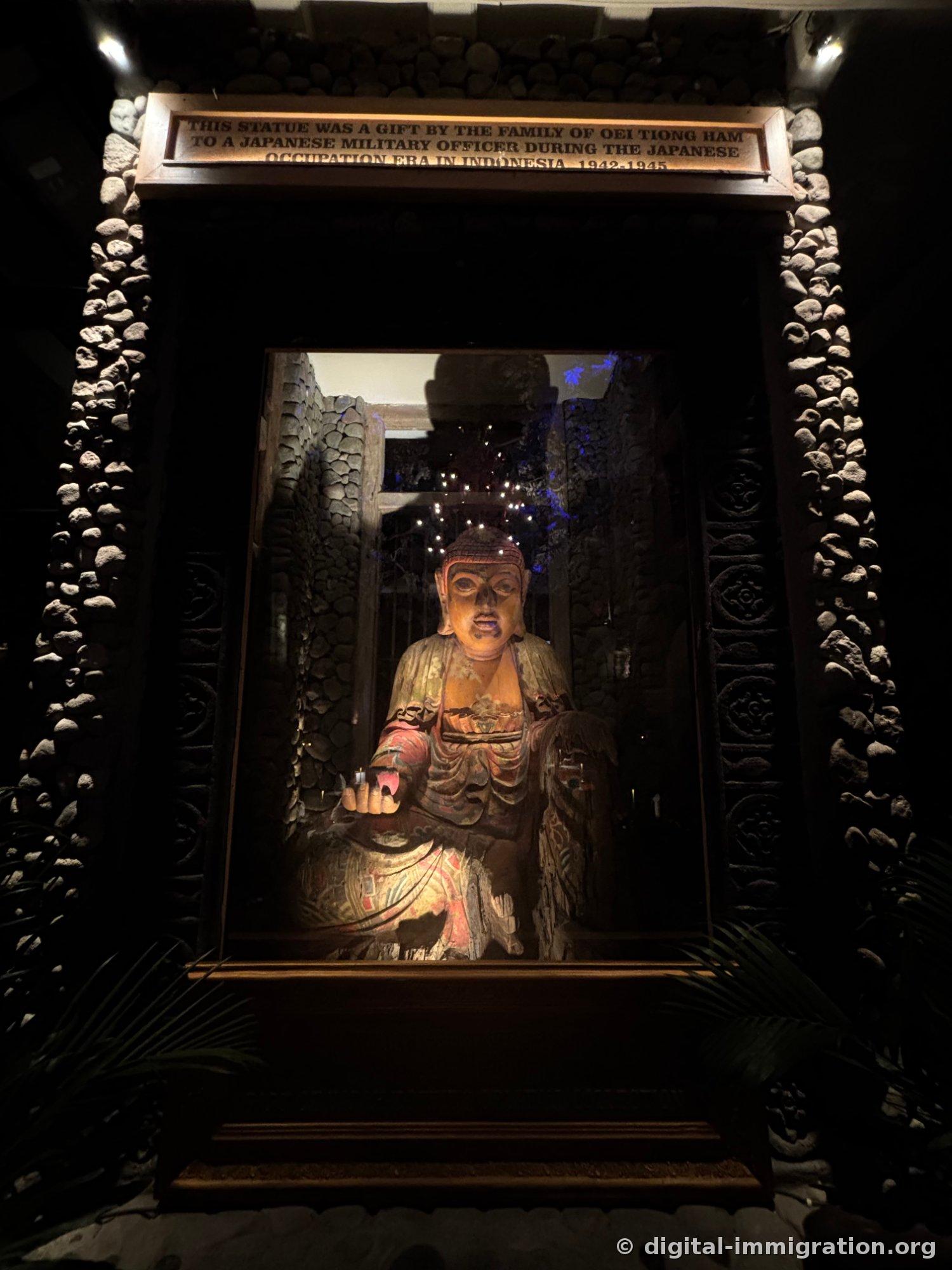 Painted wooden statue in glass case with stone-set frame and English brass description plaque above