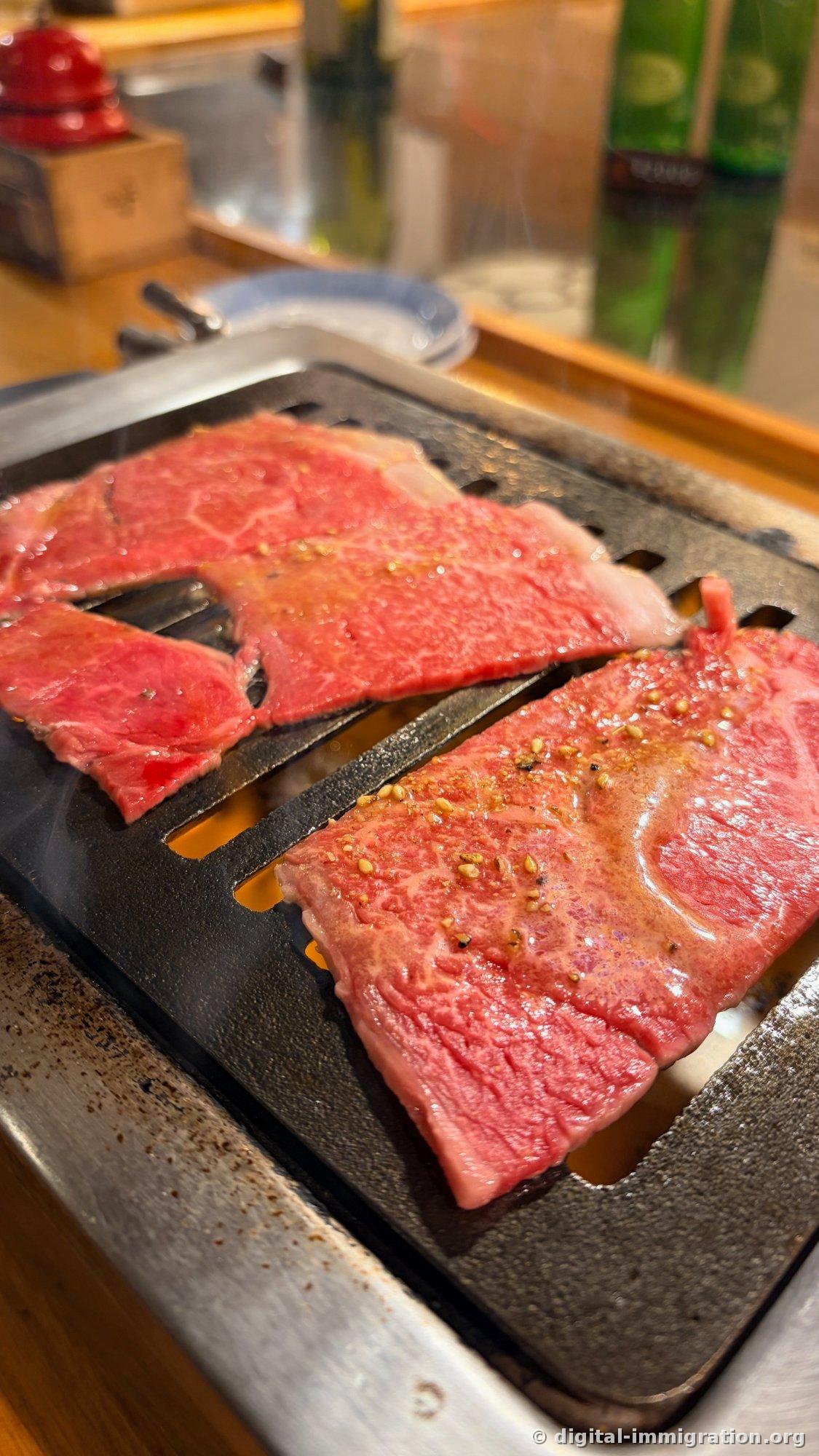 Two types of red beef on a smokeless roaster grate. The piece on the right has sesame and coarse pepper sprinkled on it, with smoke rising