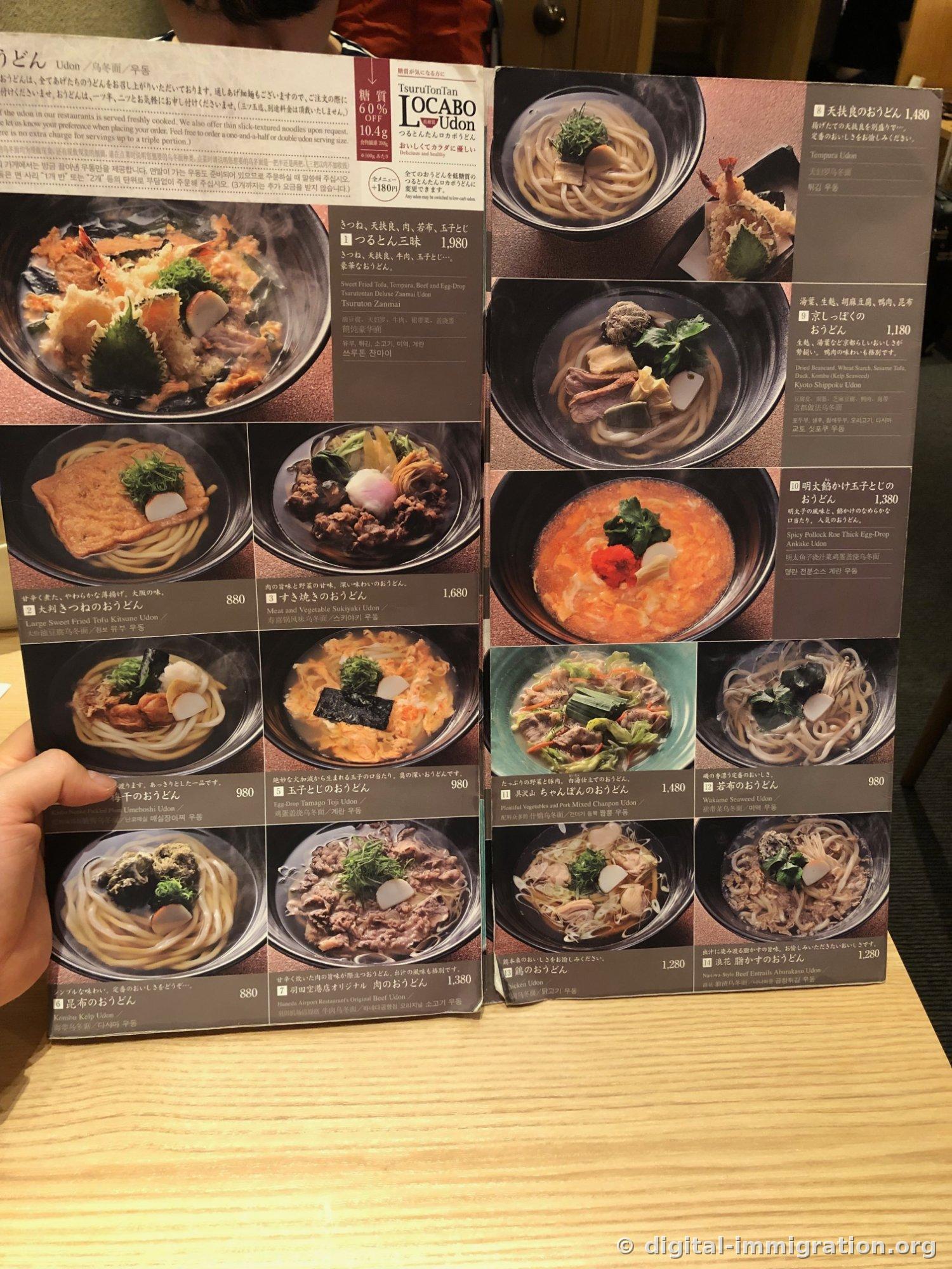 Open spread of Tsurutontan udon menu with numbered items and descriptions in four languages, showing photos and prices from item 1 (Tsuruton zanmai 1,980 yen) through item 14