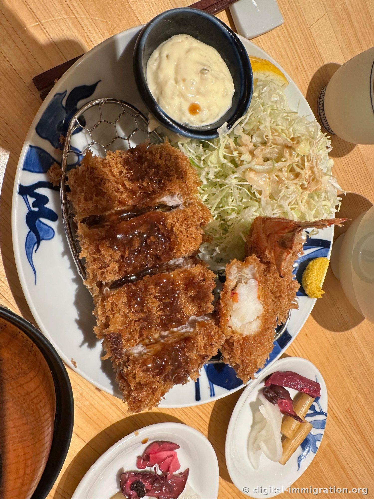 浇过酱油的里脊肉炸猪排和切开的虾炸块，盘子里还有塔塔酱碟、细切的卷心菜、芥末