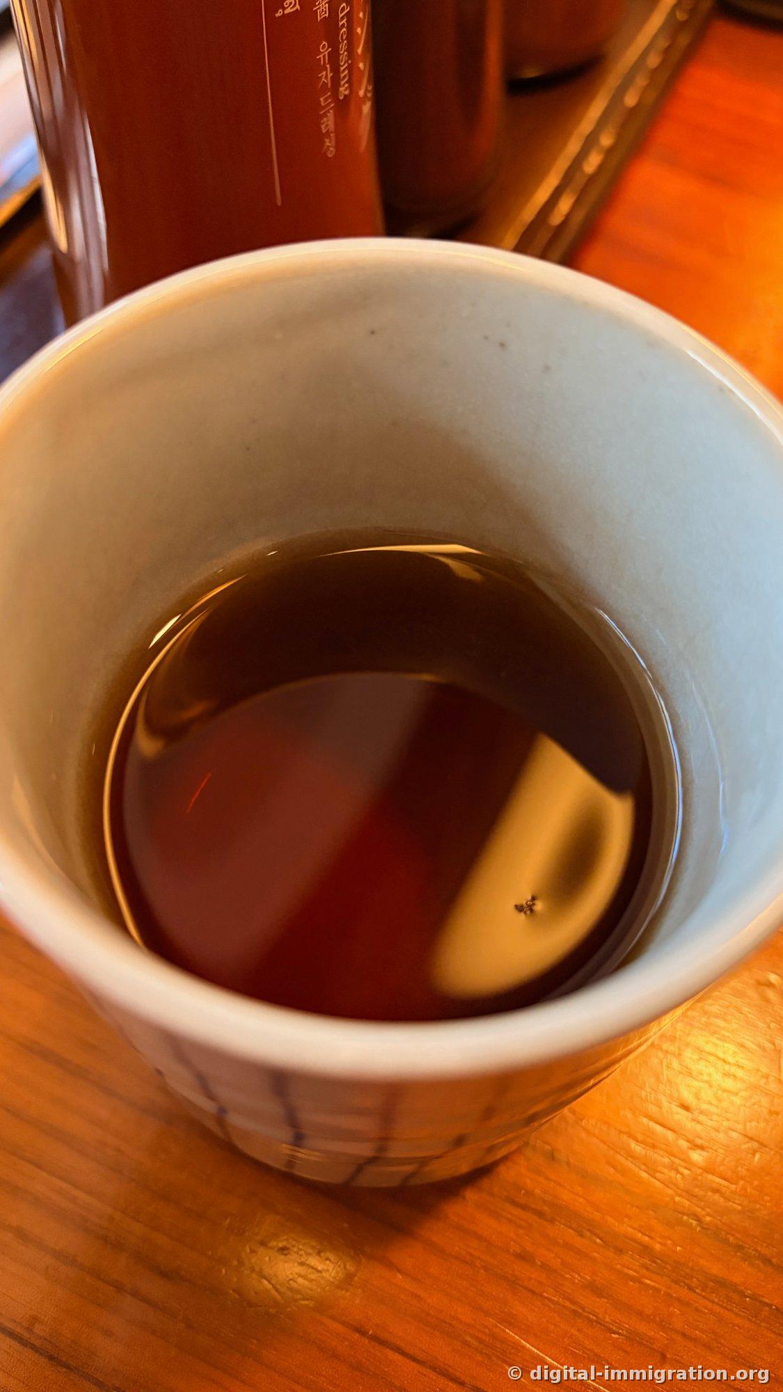 Une tasse en céramique épaisse contenant un thé foncé vue de haut. À l'arrière, on voit une bouteille avec une étiquette « Yuzu Dressing » en coréen
