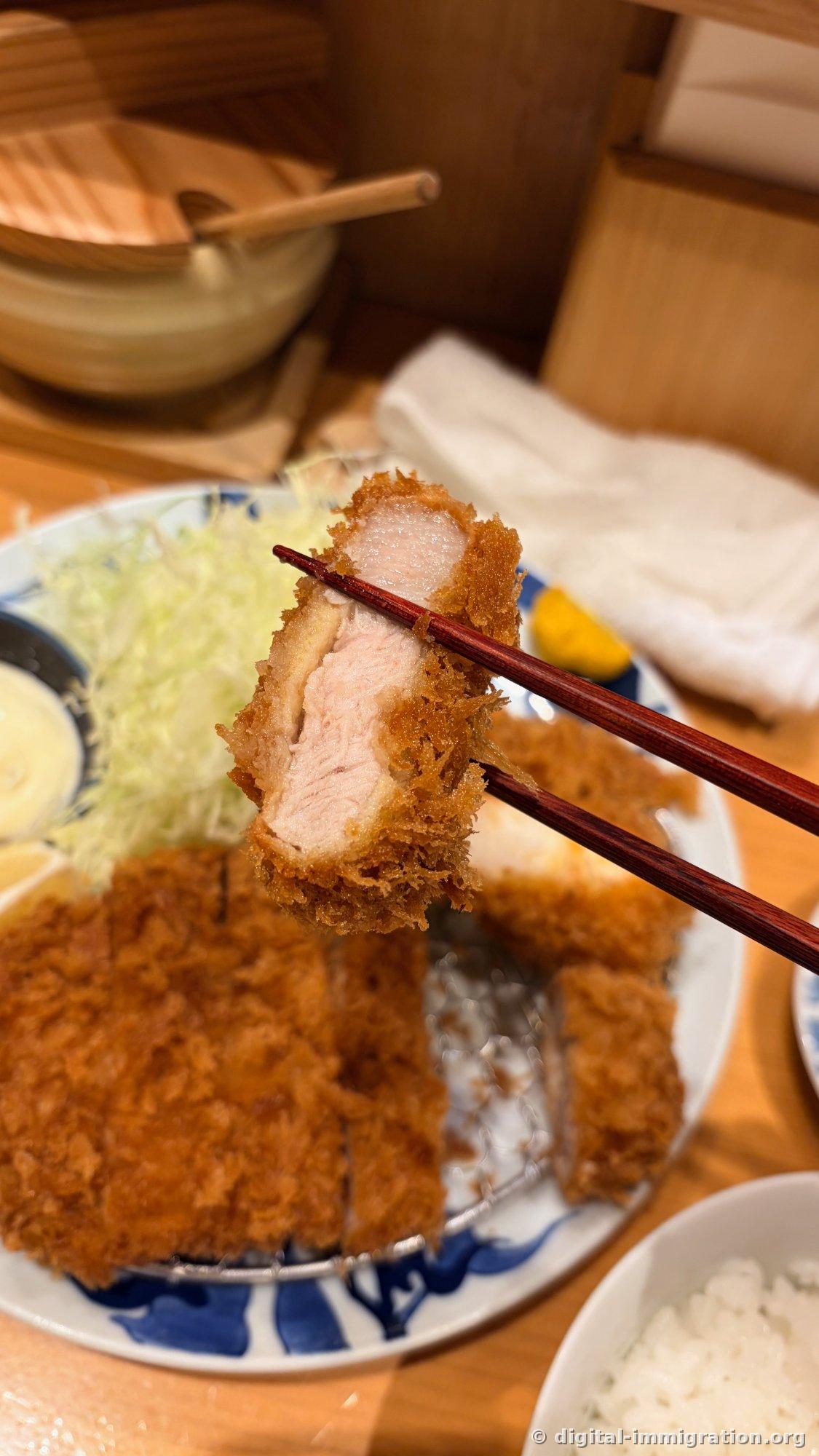 筷子上夹着的厚实里脊肉炸猪排单面，后面是木质饭筒和白色米饭碗