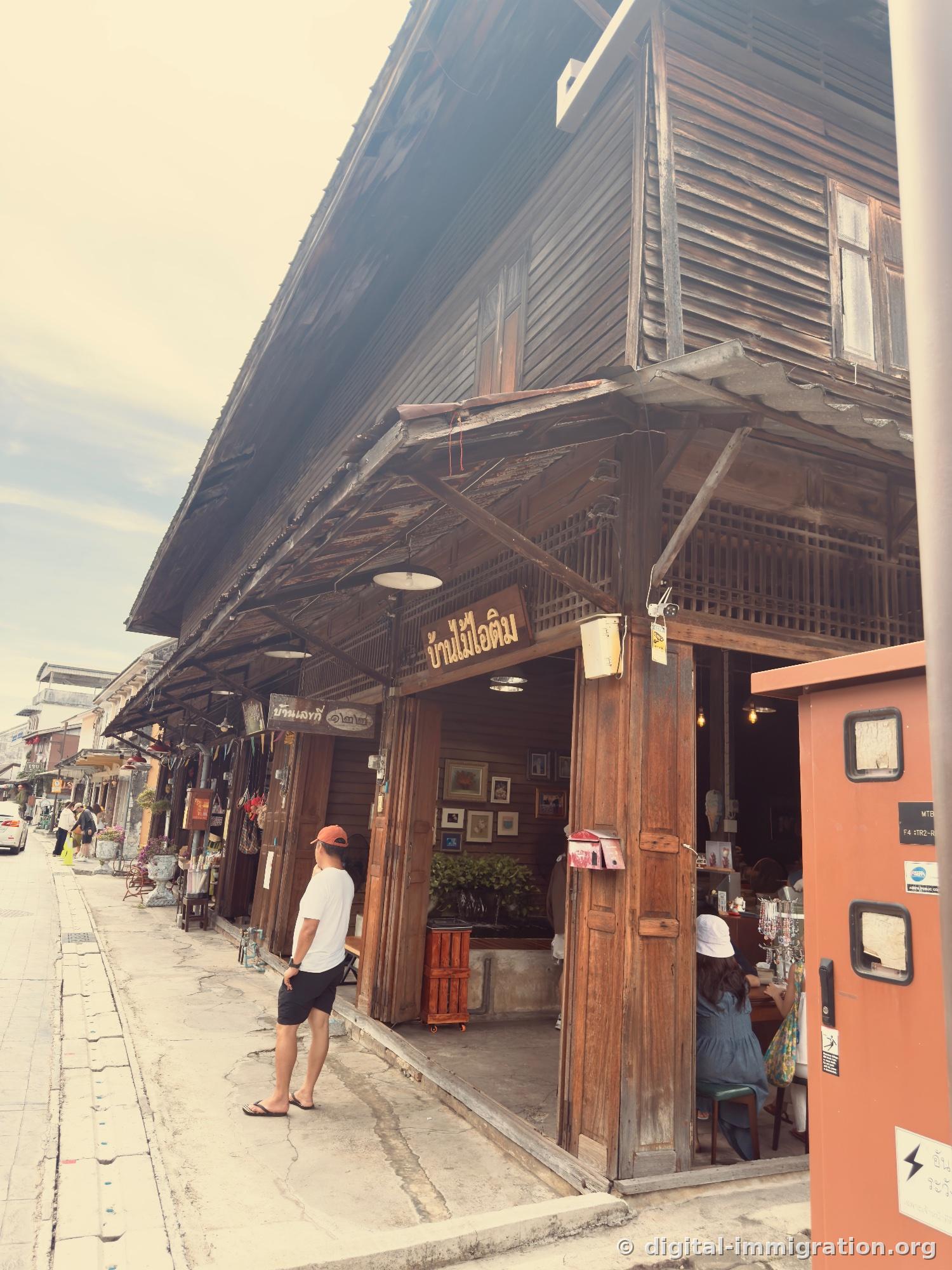 Dark wooden two-story café exterior with 'Ban Mai Ice Cream' wooden sign and man in orange hat standing in front