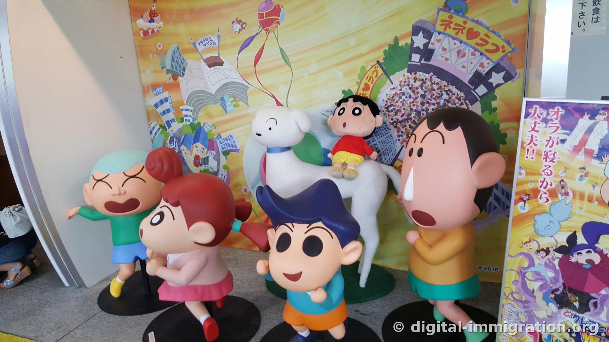 Quatre figurines de personnages secondaires de Crayon Shin-chan et une figurine de chien blanc, avec un coloré décor de film d'animation à l'arrière et une affiche de film vertical à droite