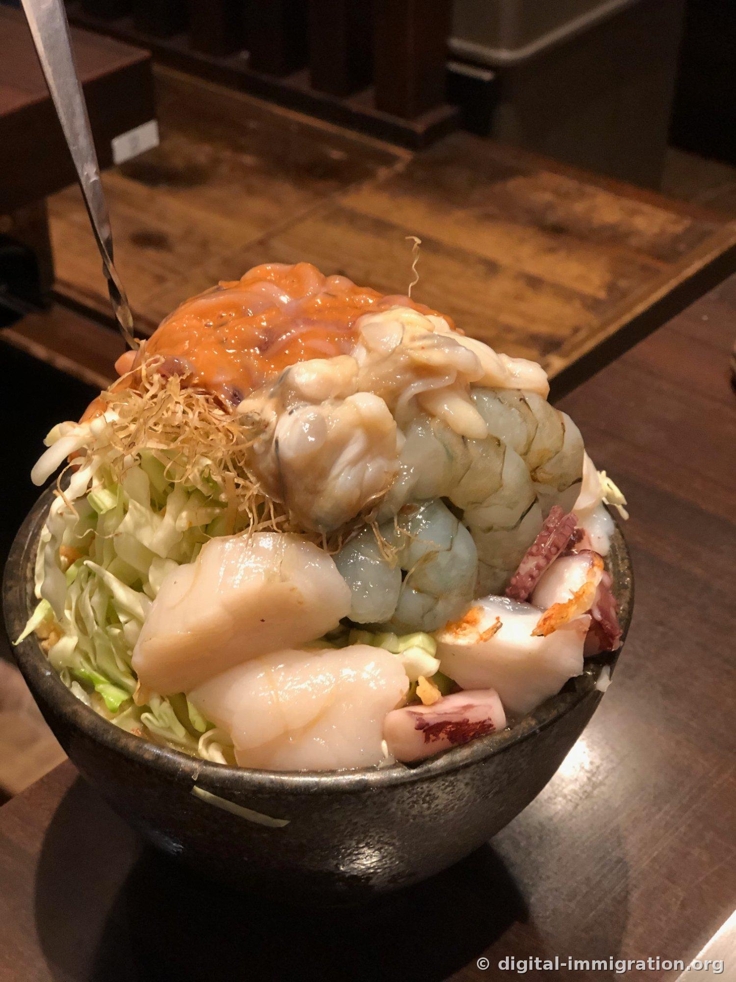 밤 늦은 츠키시마 상점가. 가게 앞에 파란 스툴이 포개져 있고 벤치가 비어 있으며 유모차를 끄는 사람이 지나간다