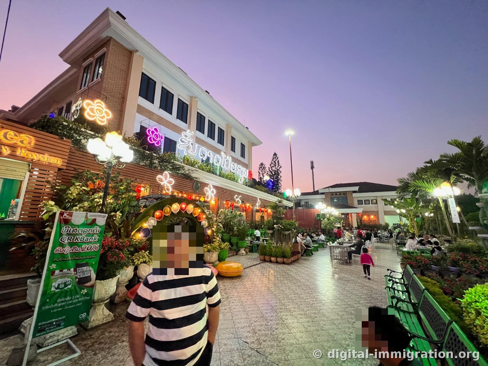 A building with Lao neon signs and the English sign 'Poysian' lit up under a pink sunset, with a KBank QR payment 20% discount advertisement sign in front