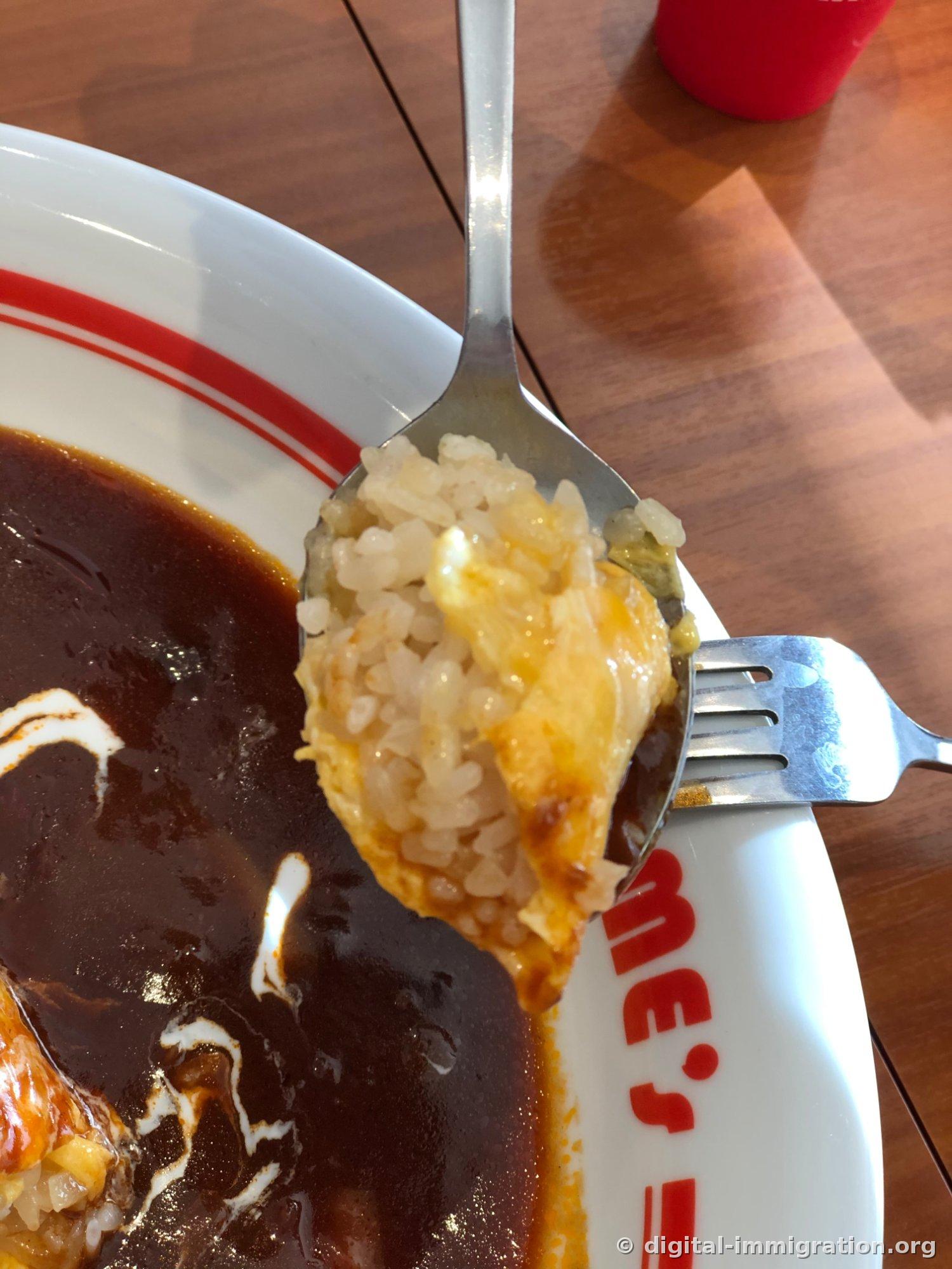 Une bouchée d'omurice sur une cuillère. Le riz jaune au beurre et l'œuf encore semi-cuit sont visibles ensemble