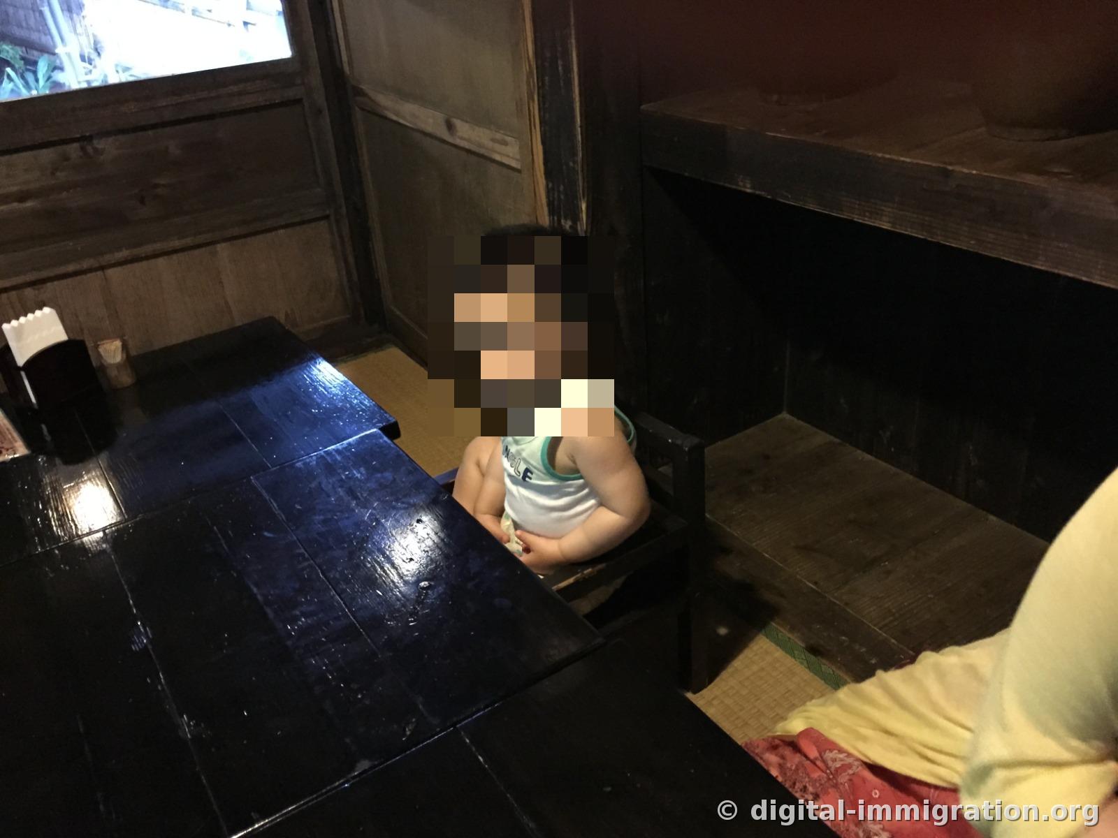 검은 나무 좌식 테이블 옆 다다미 위에 아기가 나무 아기 의자에 앉아 있는 실내 모습