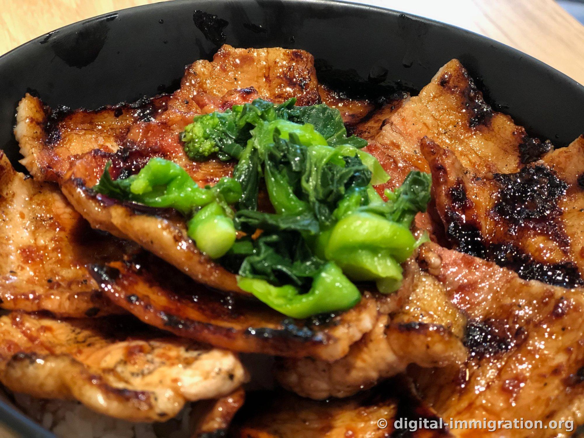 Gros plan du bol de porc. Les bords noircis par le feu et la surface brillante d'huile de la viande de porc, avec les légumes verts au centre clairement visibles